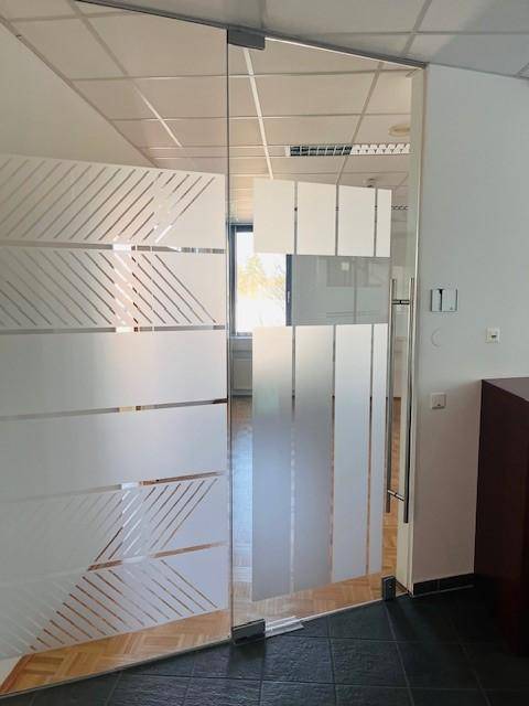Glastür mit Milchglasstreifen, die zu einem hellen Büro mit Parkettboden führt.