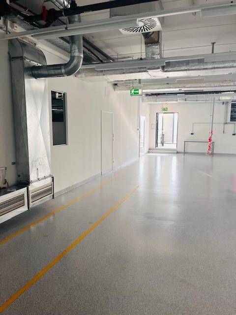 Helle Industriehalle mit Betonboden, gelben Markierungen und sichtbaren Lüftungsrohren an der Decke.