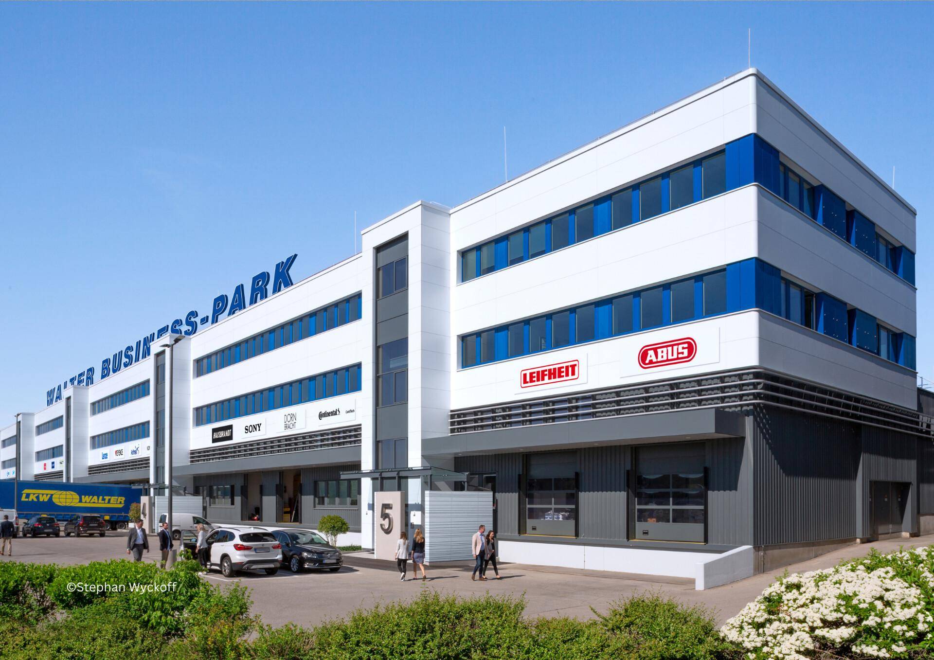 Moderne Fassade des Walter Business-Parks mit Eingangsbereich, Parkplätzen und Firmenlogos.