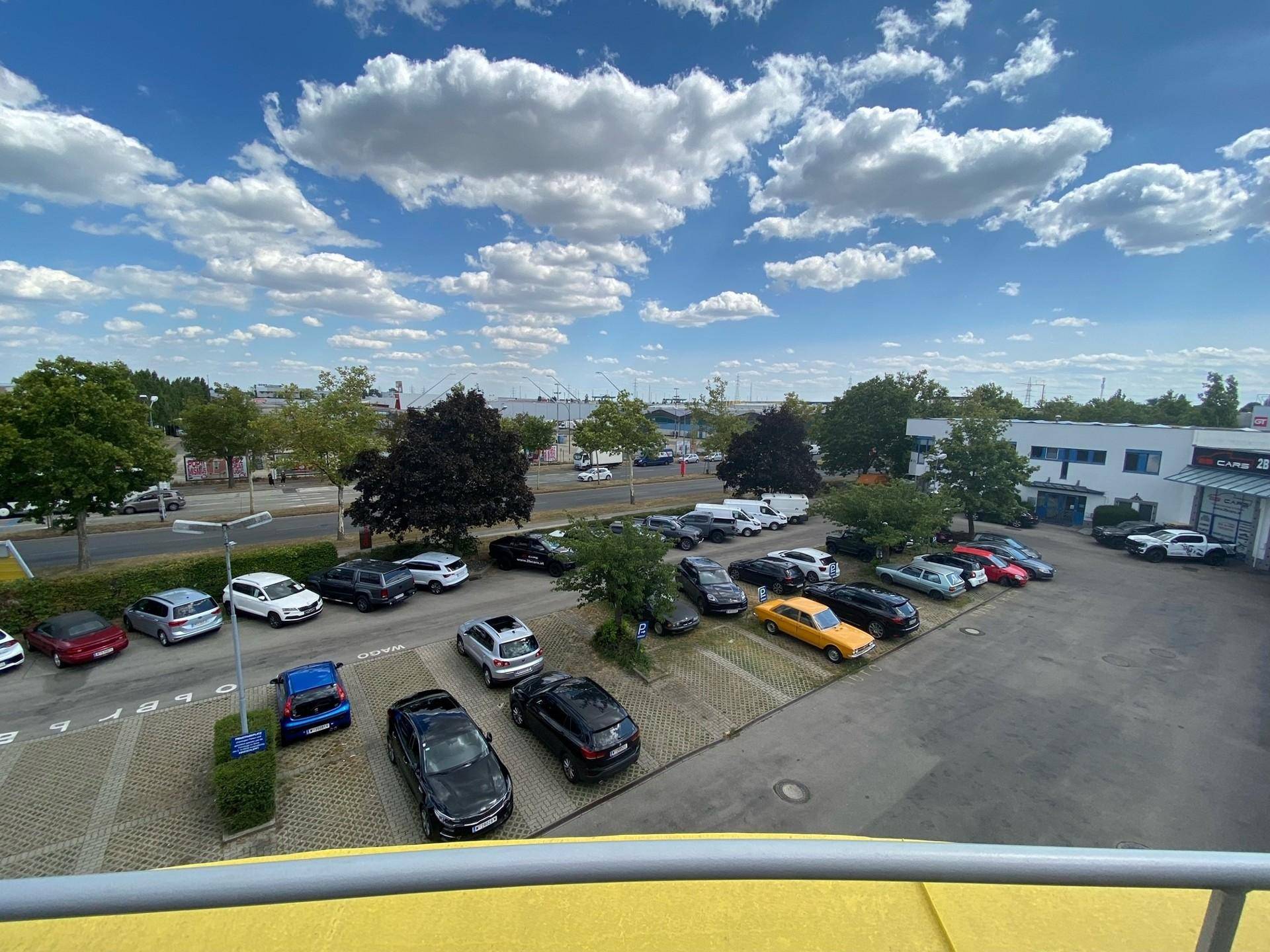 Außenansicht eines Parkplatzes mit vielen Autos unter blauem Himmel und Wolken.