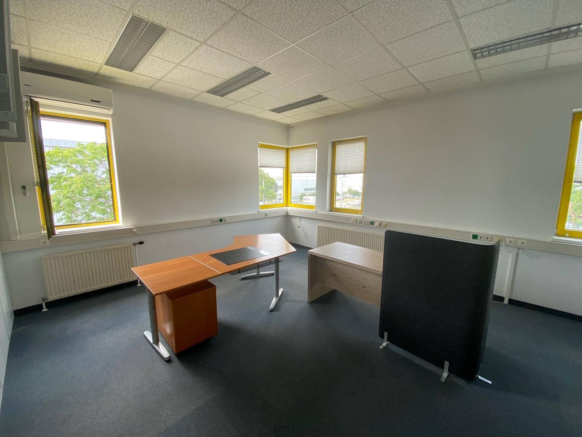 Möbliertes Einzelbüro mit zwei Schreibtischen, Teppichboden und Klimaanlage, hell durch große Fenster.