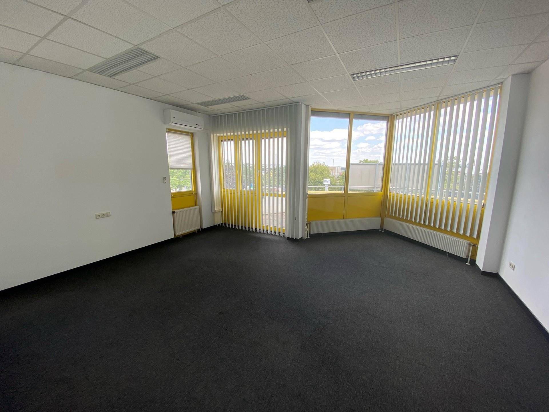 Helles Büro mit dunklem Teppichboden, großen Fenstern und vertikalen Jalousien, ausgestattet mit Klimaanlage.