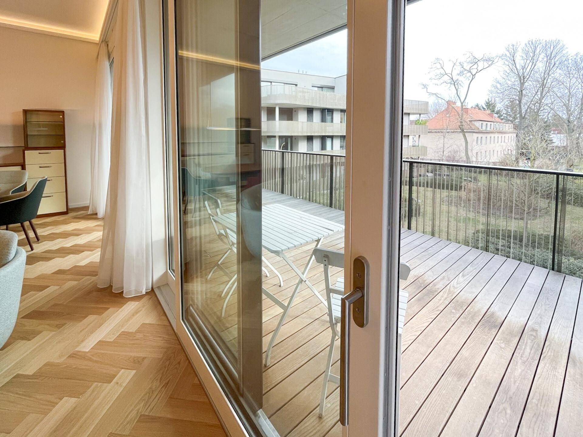Große Glasschiebetür vom Wohnzimmer zum Balkon mit Holzboden und Blick ins Grüne.