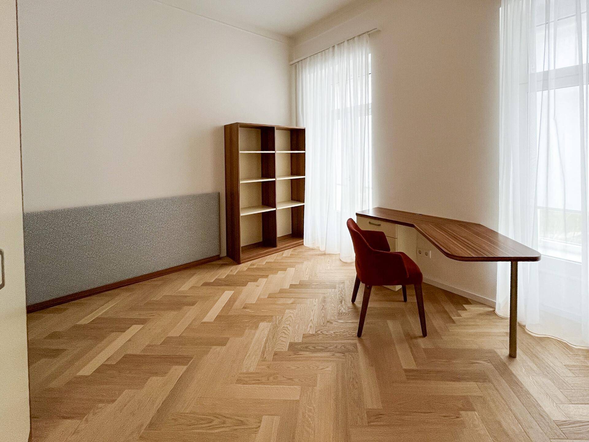 Helles Arbeitszimmer mit Fischgrätparkett, großem Fenster und modernem Schreibtisch.