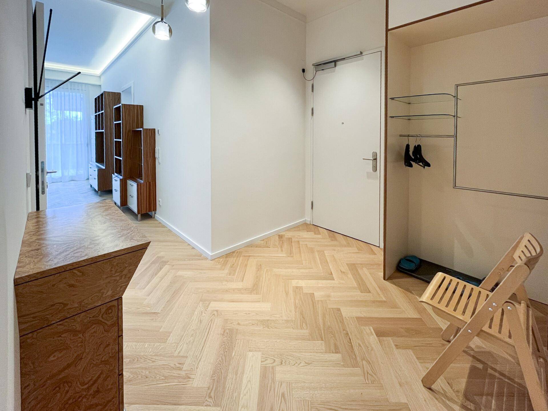 Heller Eingangsbereich mit Fischgrätparkett und Garderobenschrank, führt in den Wohnbereich.