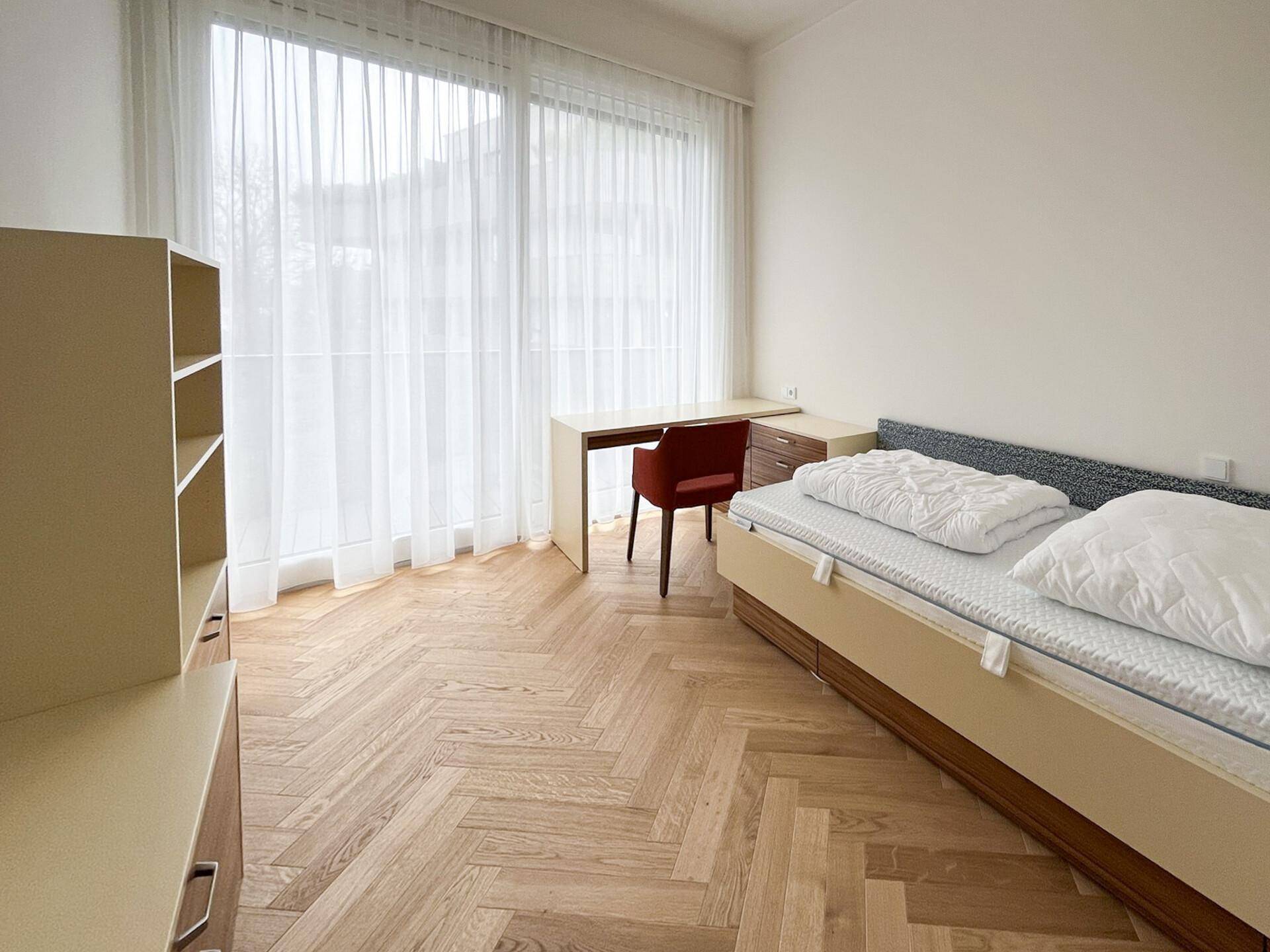 Schlafzimmer mit Fischgrätparkett, großem Fenster und Zugang zum Balkon.