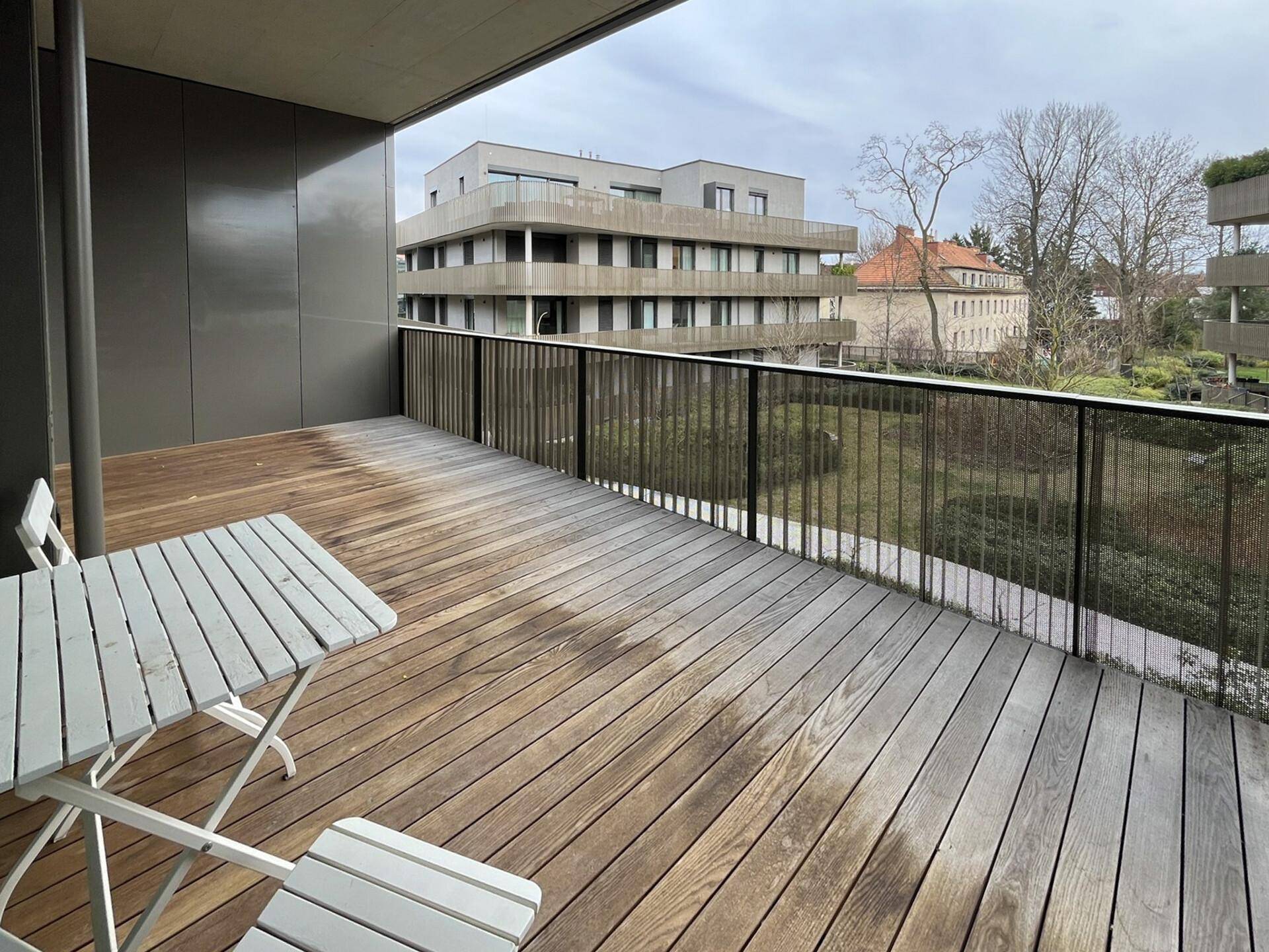Geräumiger Balkon mit Holzboden und Blick auf die gepflegte Grünanlage der Wohnanlage.