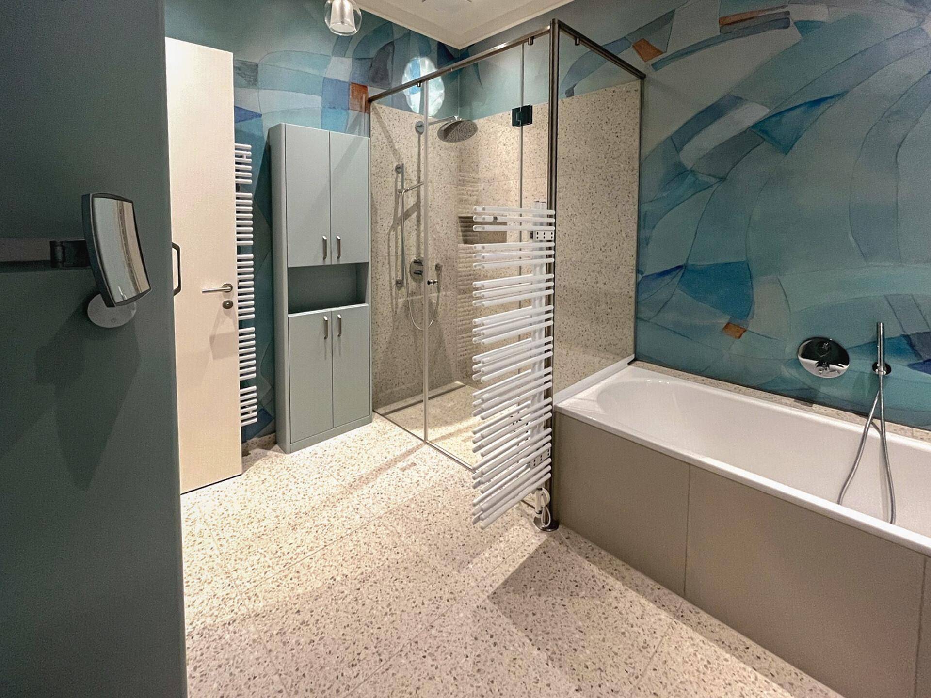 Geräumiges Badezimmer mit Badewanne, großer Dusche und beheiztem Handtuchhalter.