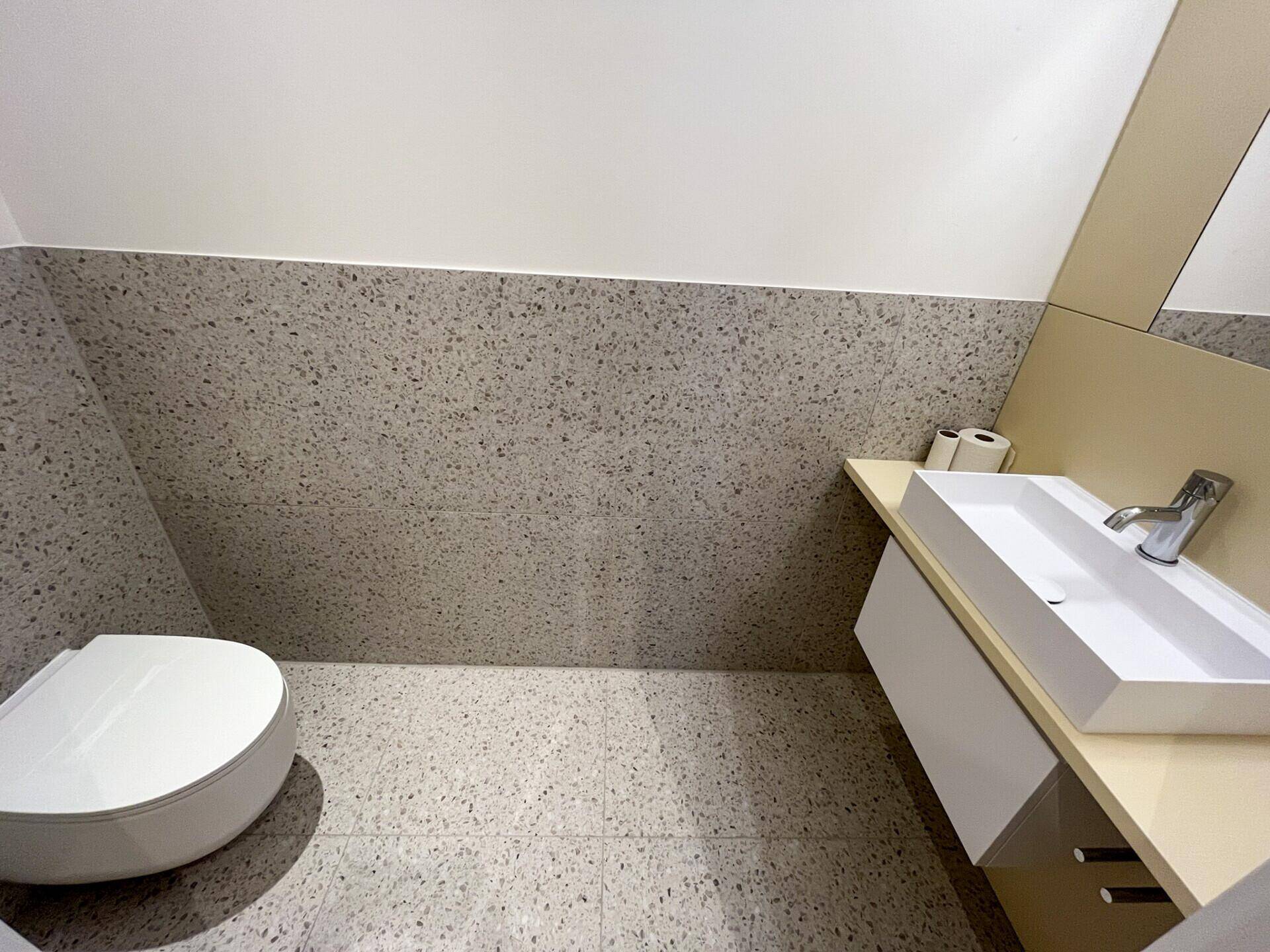 Modernes Gäste-WC mit wandhängendem WC und Einzelwaschbecken, in neutralen Farben gehalten.