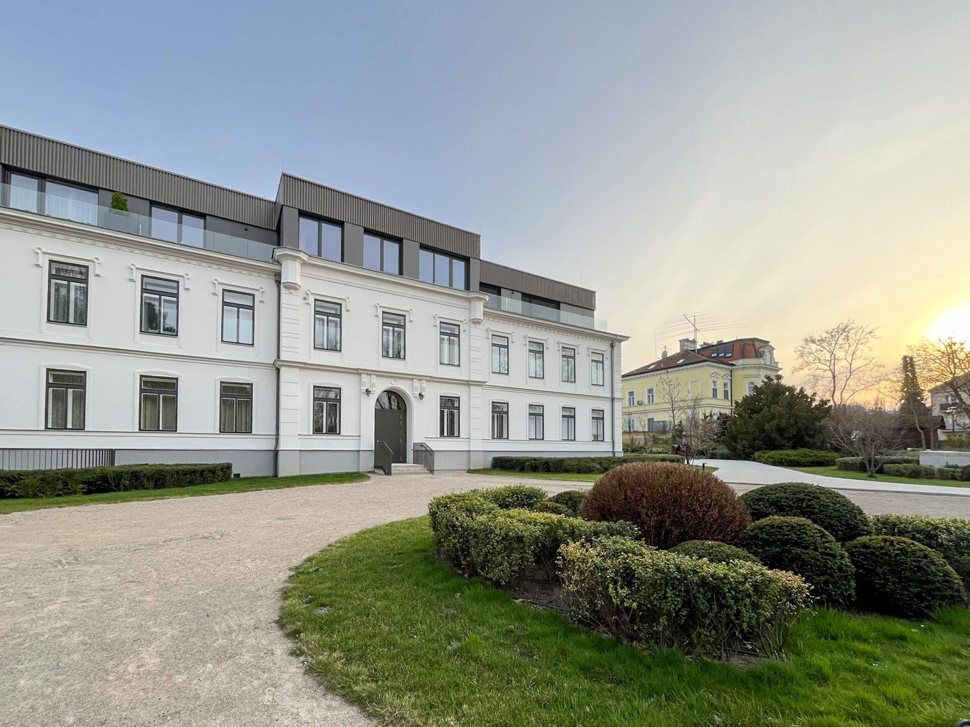 Elegantes Altbaugebäude mit moderner Dachaufstockung und gepflegter Außenanlage.