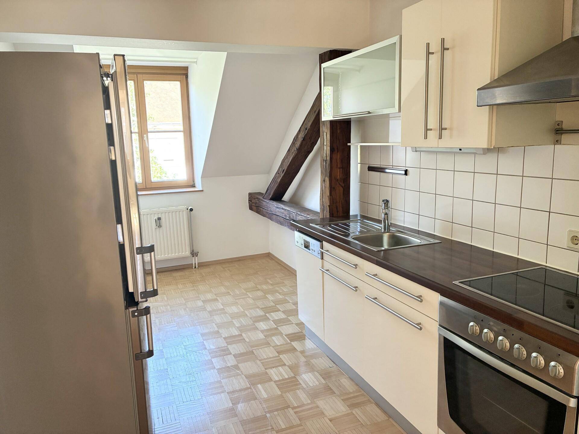 Funktionale Küche mit weißen Schränken, Einbaugeräten und Dachschrägenfenster.