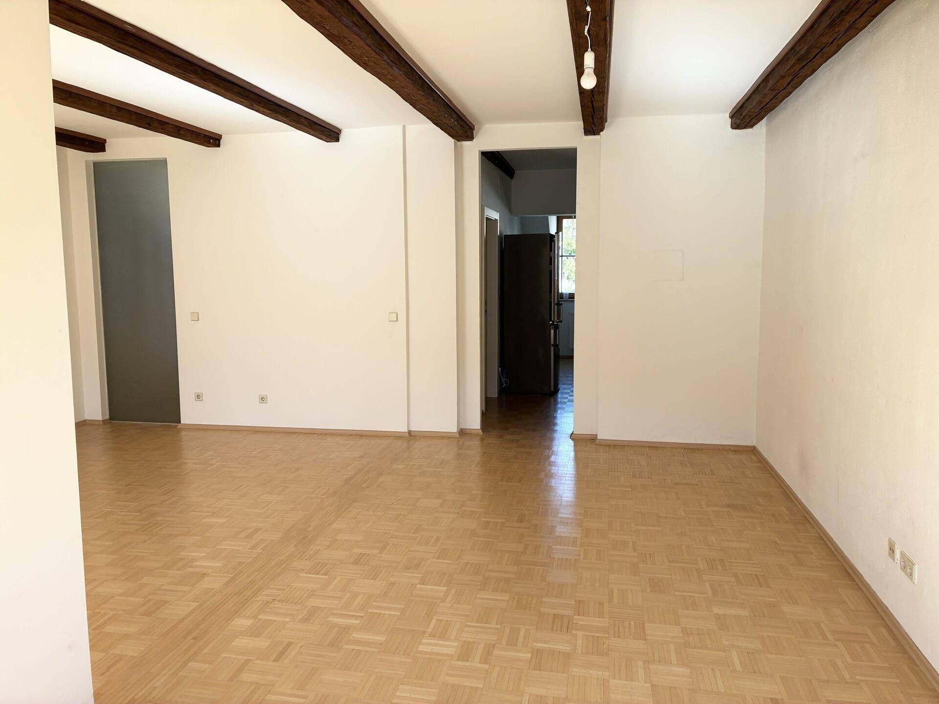 Geräumiger Wohnbereich mit Holzbalken, Parkettboden und Zugang zu weiteren Räumen.