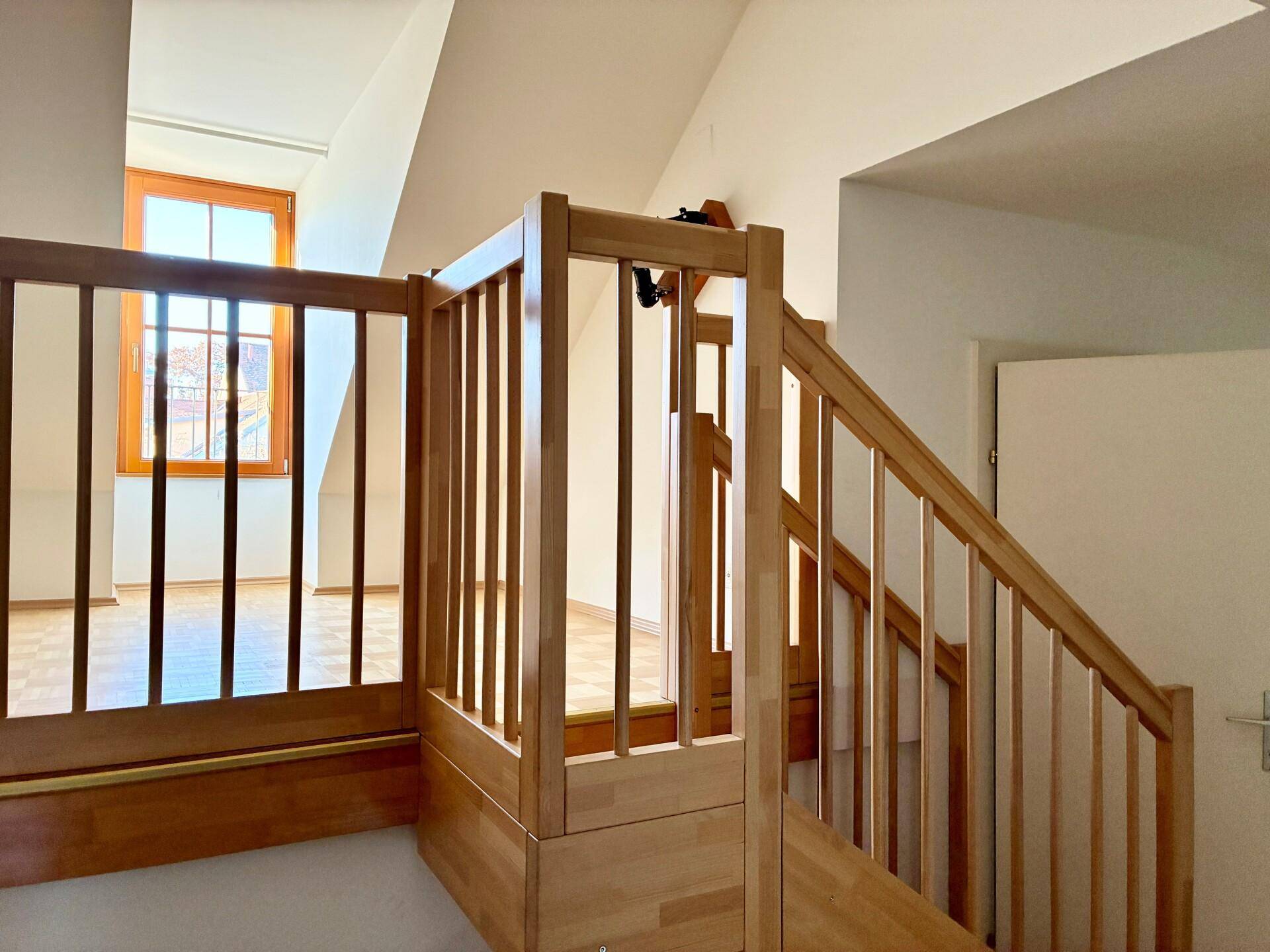 Helle Holztreppe führt in das obere Stockwerk mit Blick auf ein Fenster.