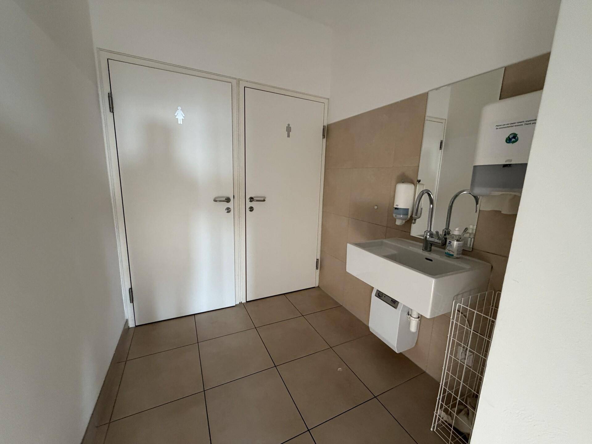 Toilettenbereich mit zwei Türen, einem Waschbecken und Fliesenboden, in gutem Zustand.