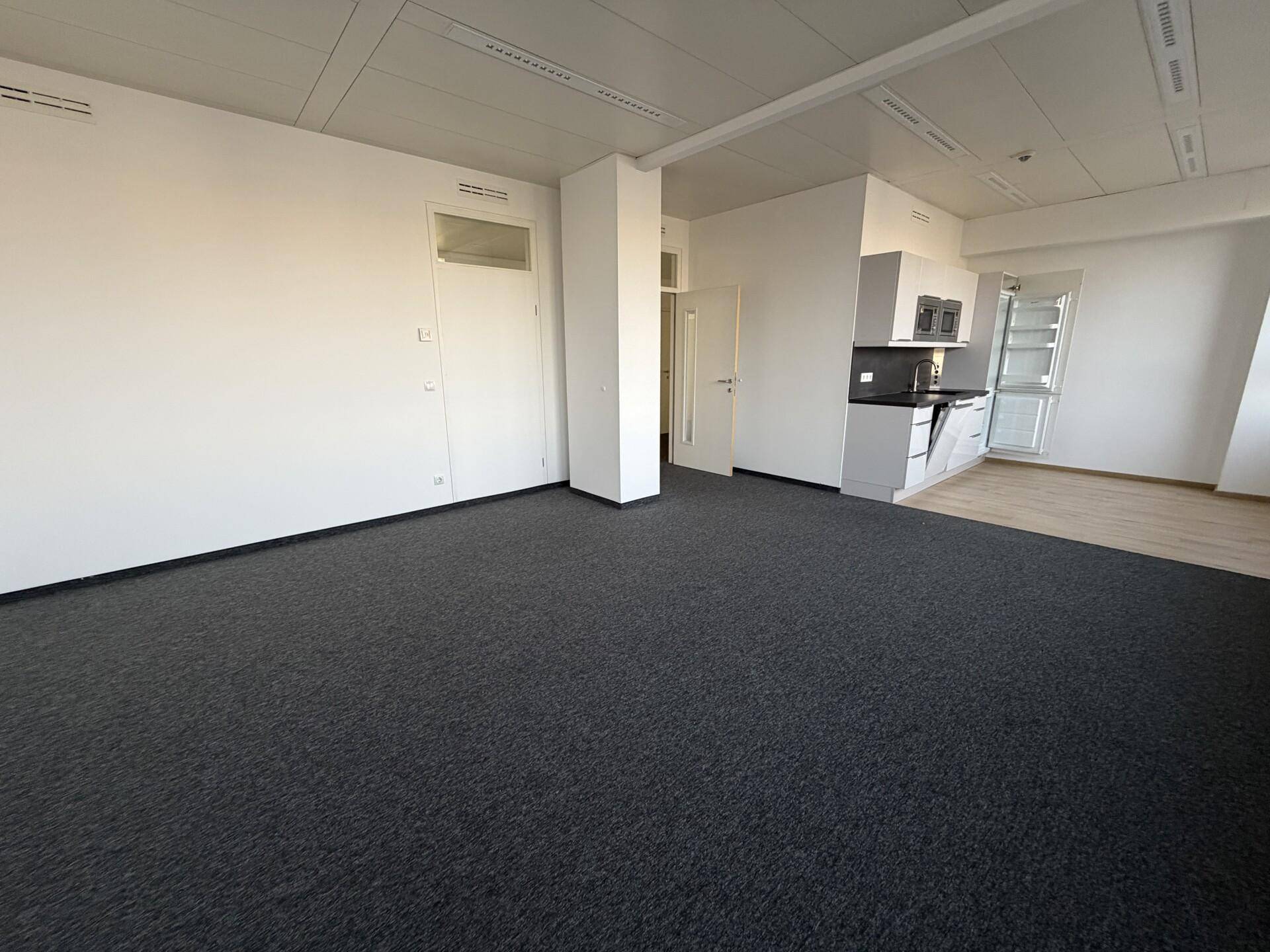 Offener Bürobereich mit Teppichboden und einer integrierten Küchenzeile mit modernen Geräten.