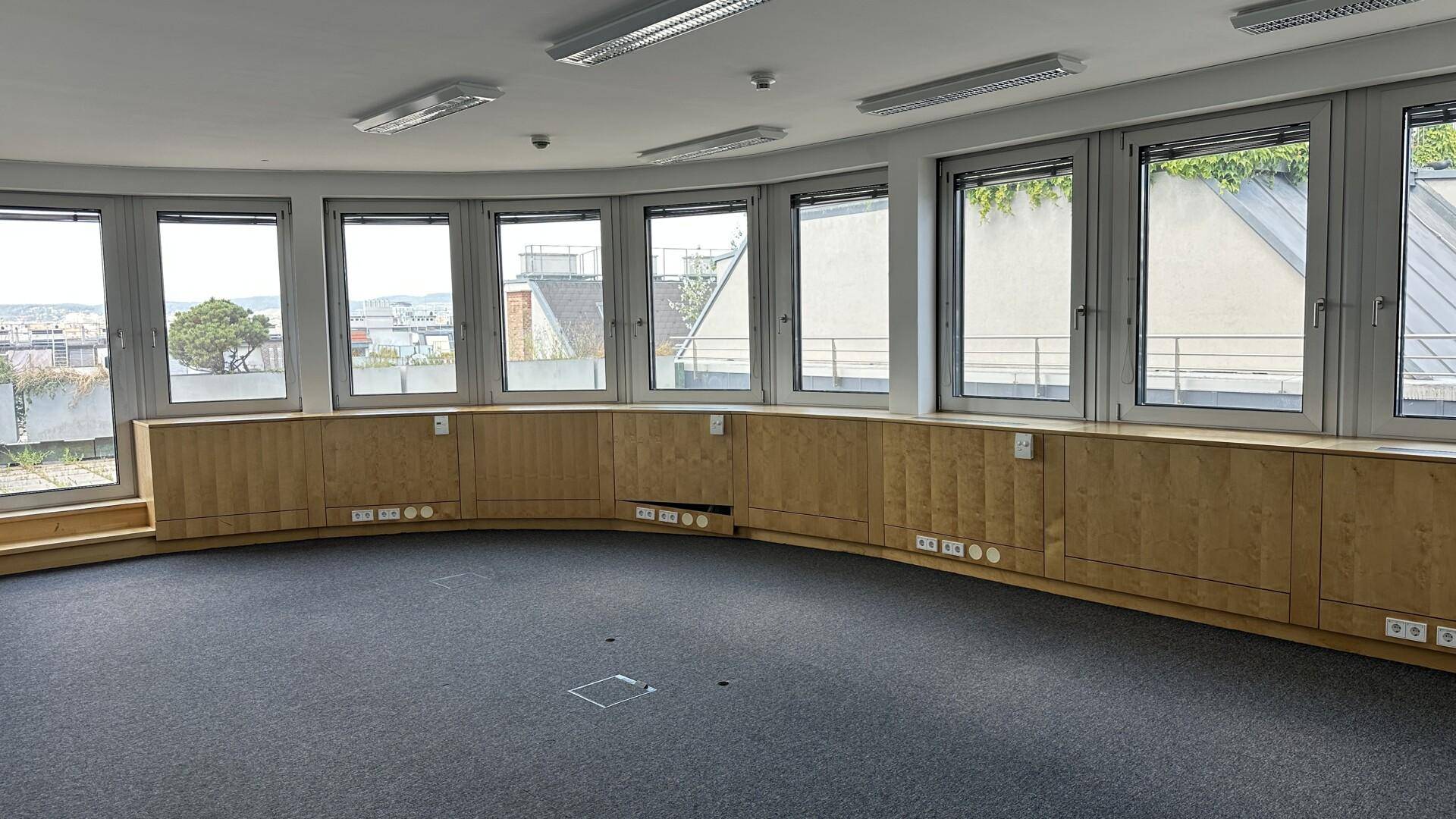 Rundes Büro mit vielen Fenstern, Teppichboden und Holzverkleidungen, bietet weite Aussicht.