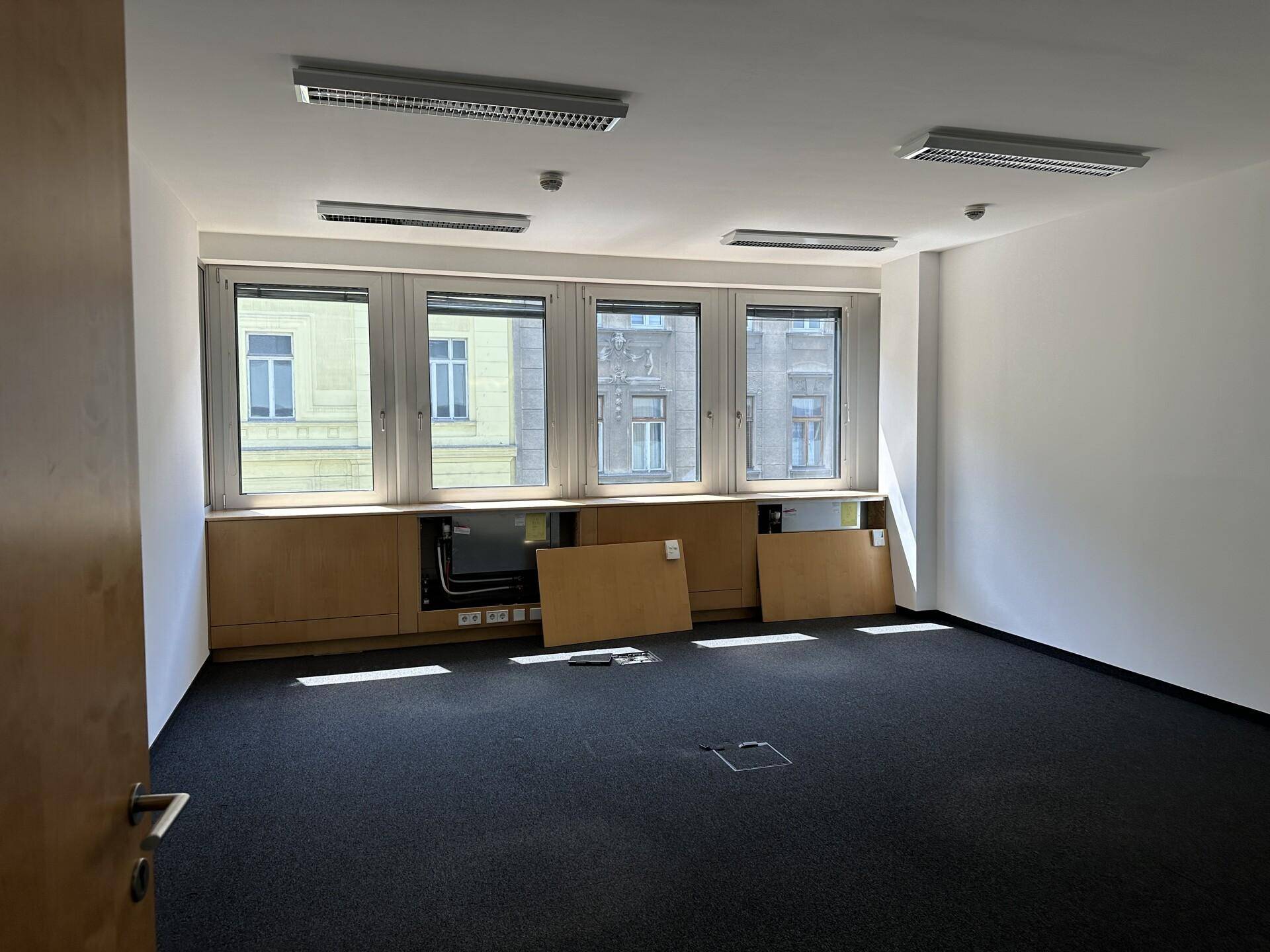 Leeres Büro mit Teppichboden, großen Fenstern und Holzverkleidungen, bereit zur Einrichtung.