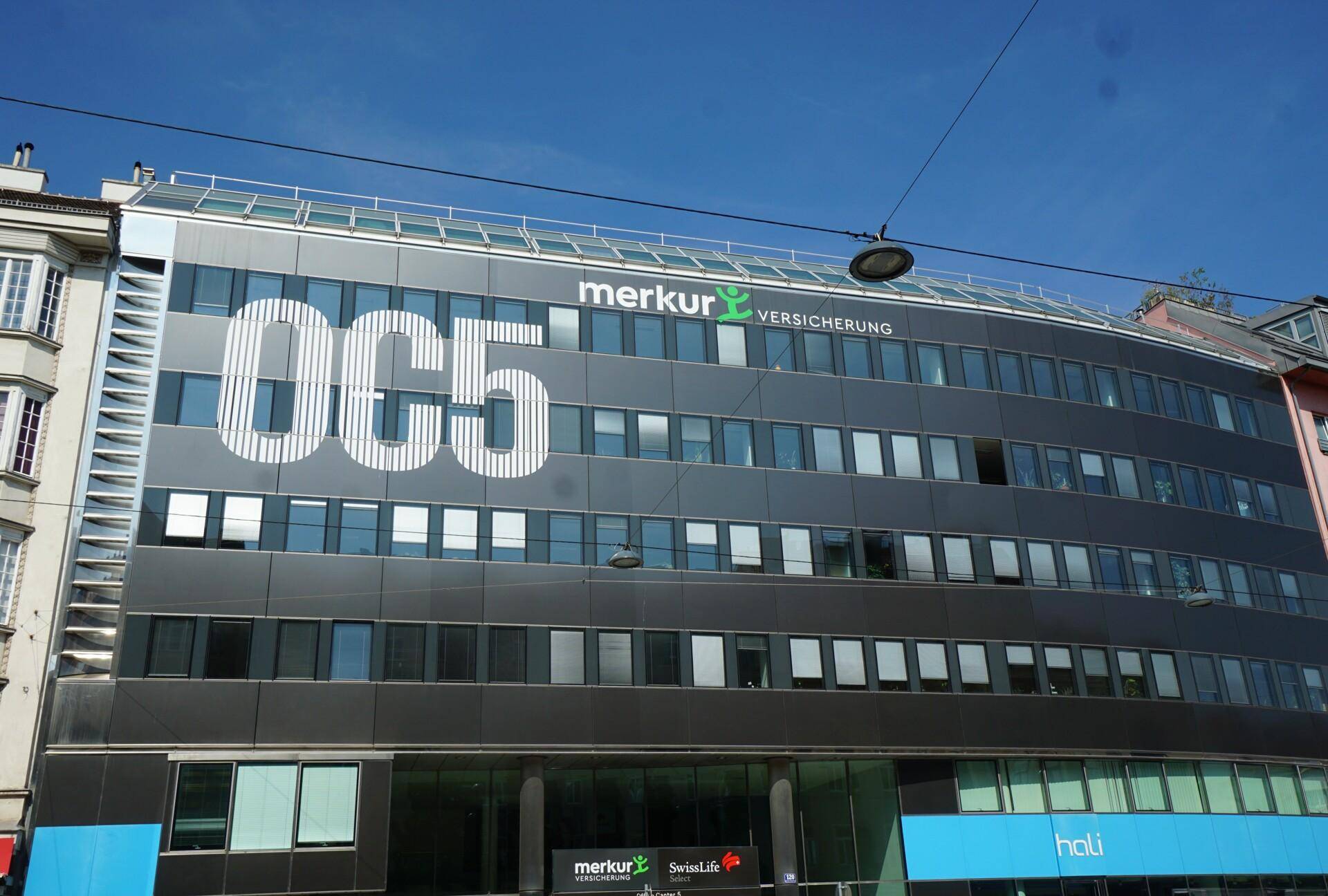 Moderne Bürogebäude-Fassade mit großen Fenstern und Firmenlogos unter blauem Himmel.