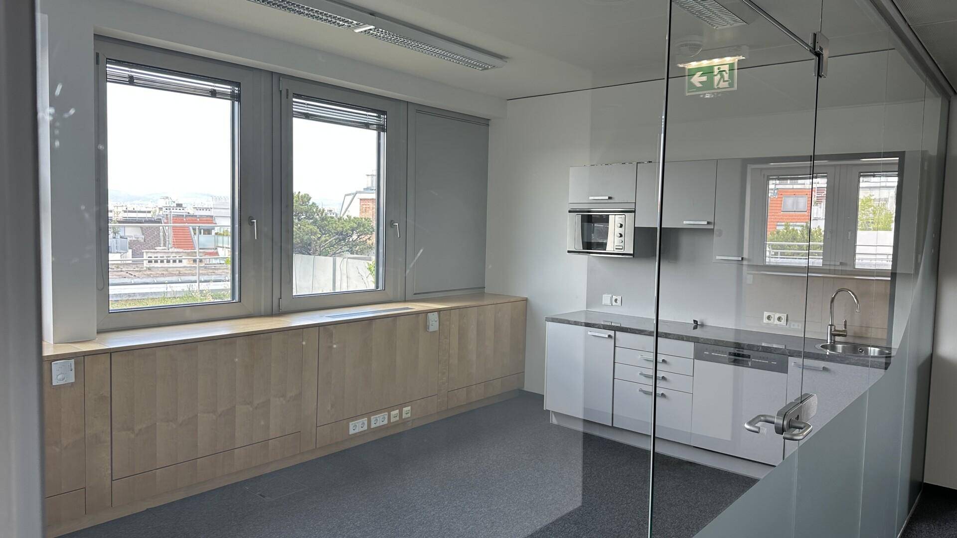 Büro mit integrierter Küchenzeile hinter einer Glaswand und Blick auf die umliegenden Dächer.