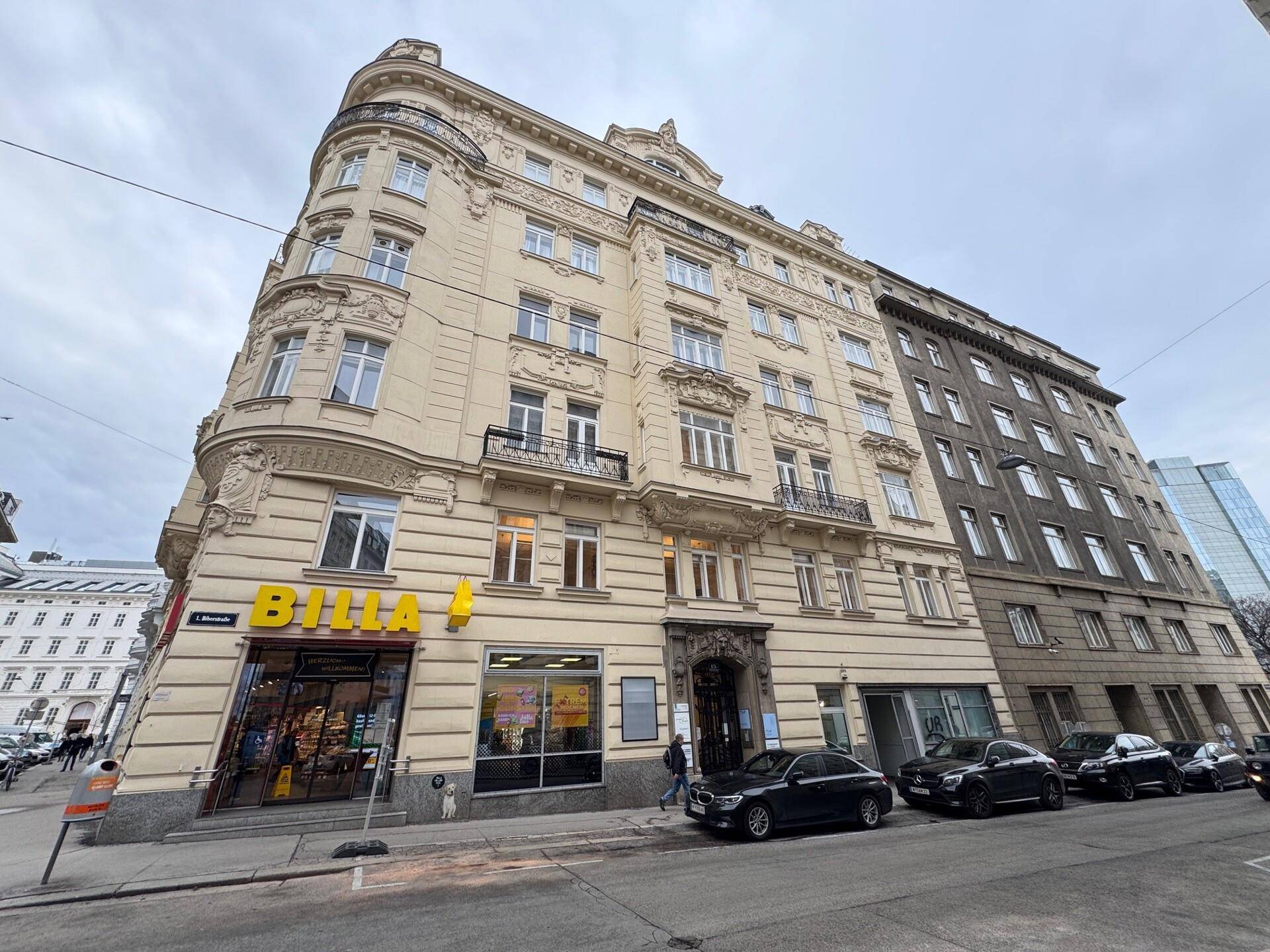 Historisches Gebäude mit reich verzierter Fassade und einem Supermarkt im Erdgeschoss an einer belebten Straße.