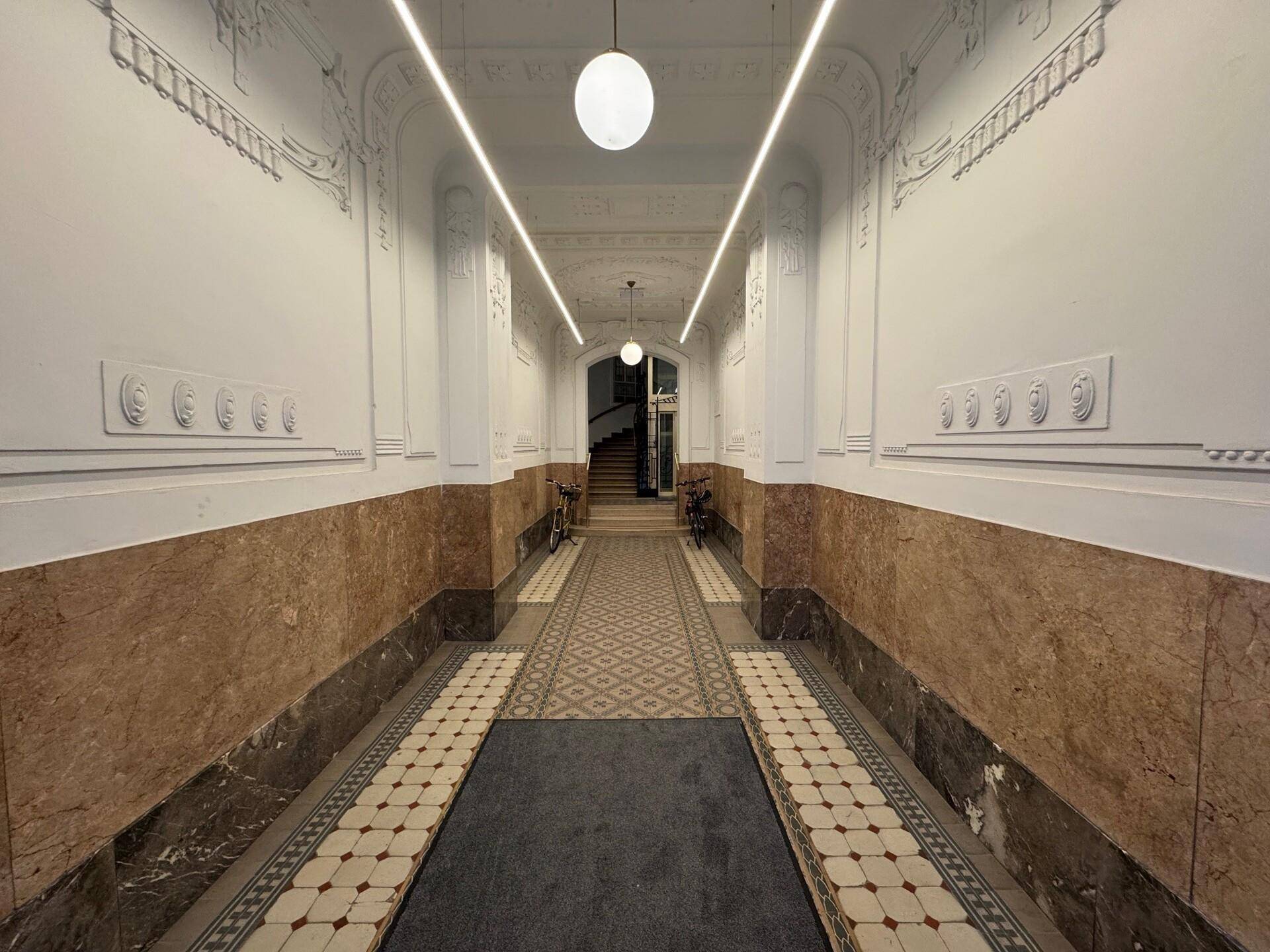 Prunkvoller Flur mit hohen Decken, Marmorverkleidung und kunstvollen Stuckelementen, der zum Treppenhaus führt.