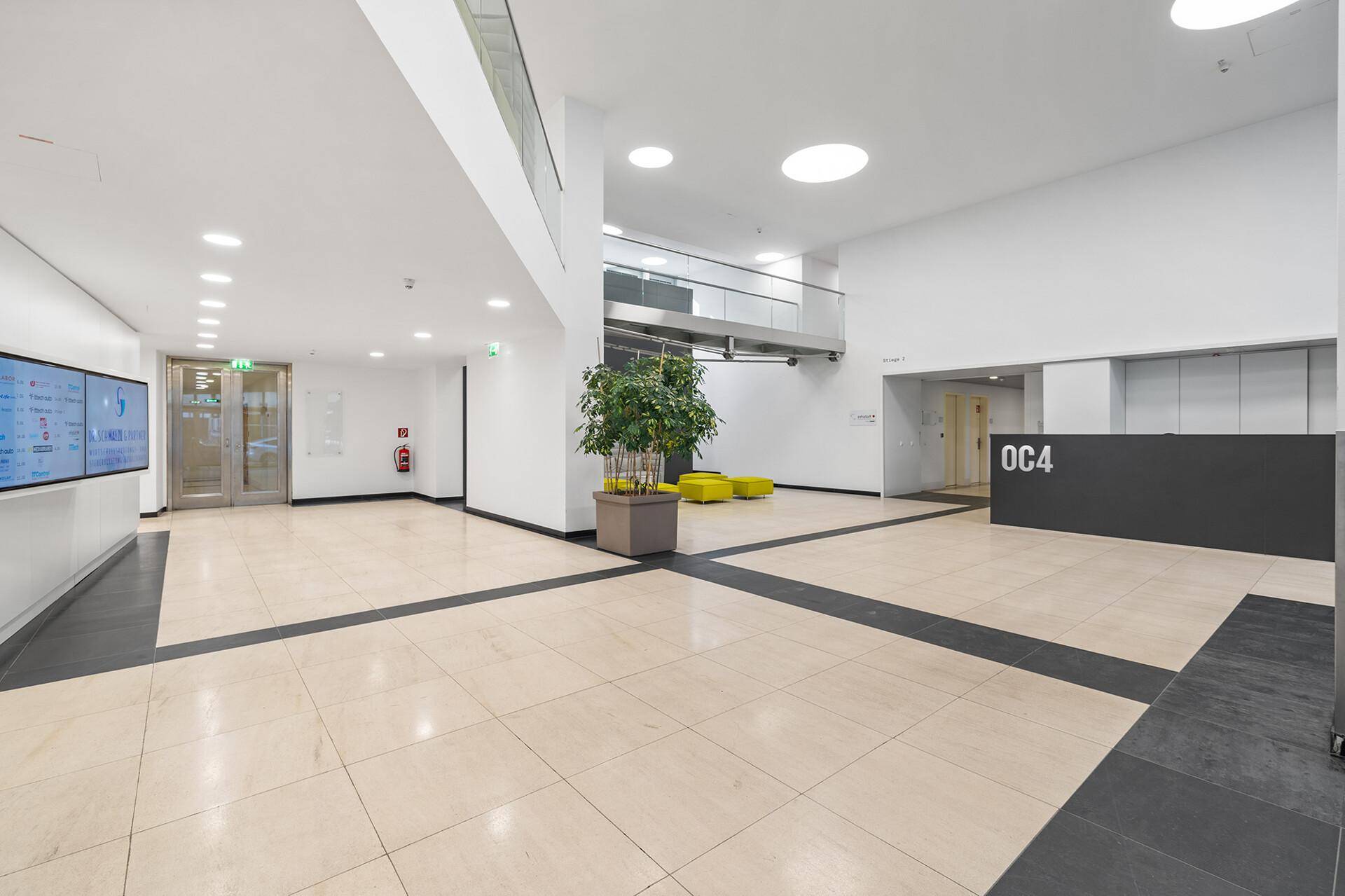 Geräumige und helle Lobby mit Fliesenboden, Empfangsbereich und einer Pflanze in der Mitte des Raumes.