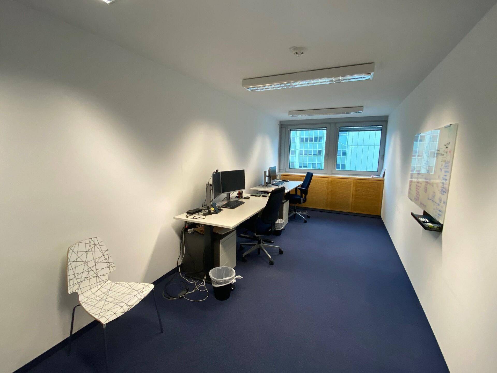 Kompaktes Büro mit zwei Arbeitsplätzen, Computern und einem Fenster, das für ausreichend Helligkeit sorgt.