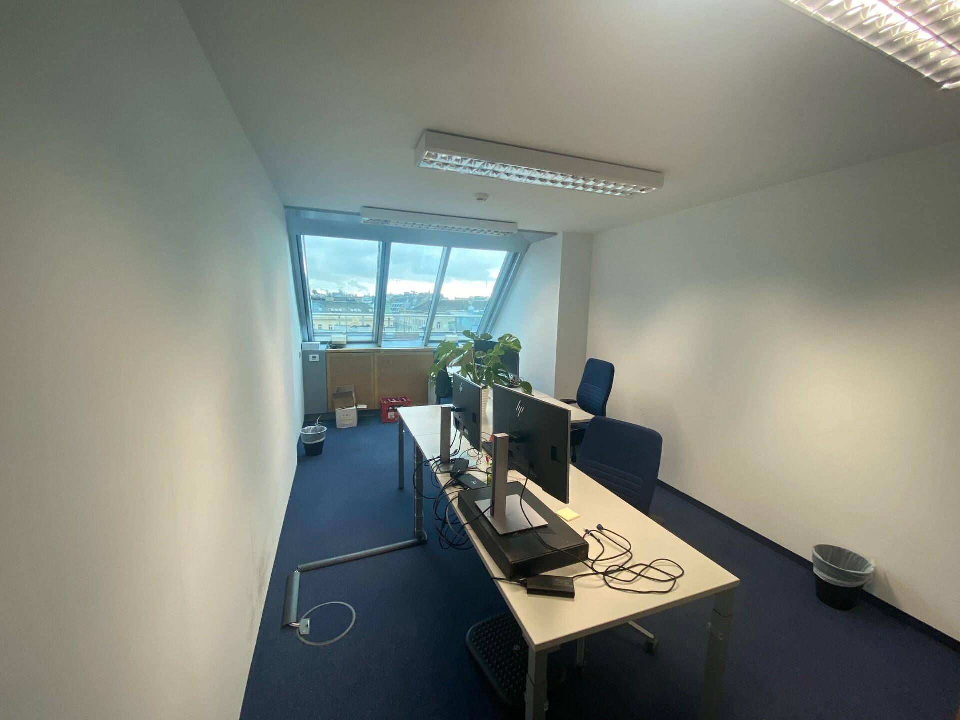 Einzelbüro mit einem Arbeitsplatz, Computer und schrägen Fenstern, die viel Tageslicht hereinlassen.