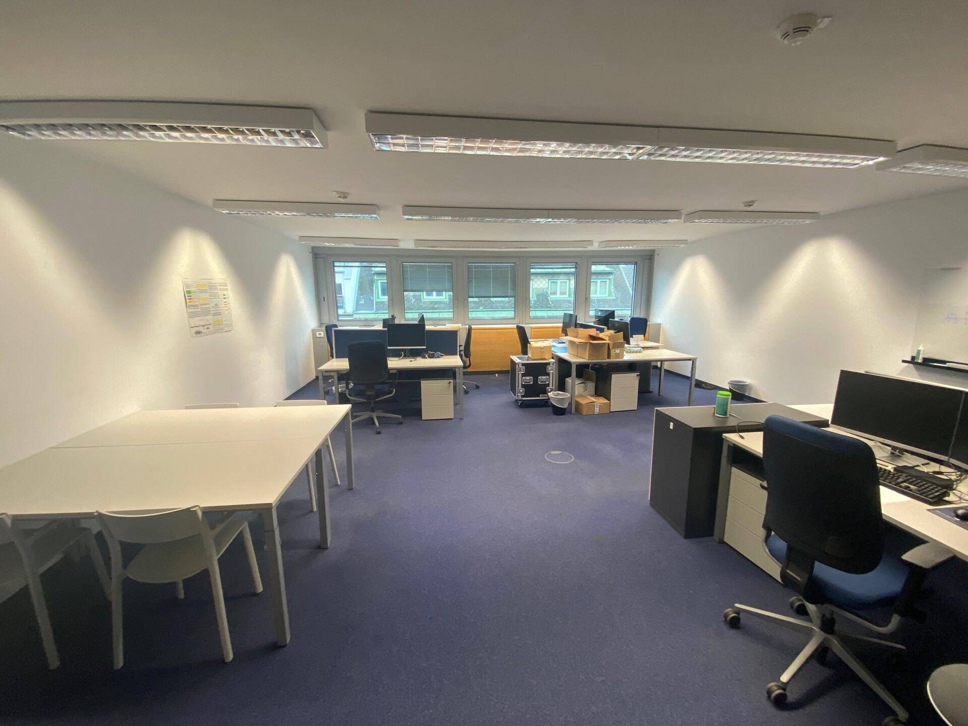 Geräumiges Großraumbüro mit mehreren Arbeitsplätzen, Computern und Fenstern, die eine produktive Arbeitsumgebung schaffen.