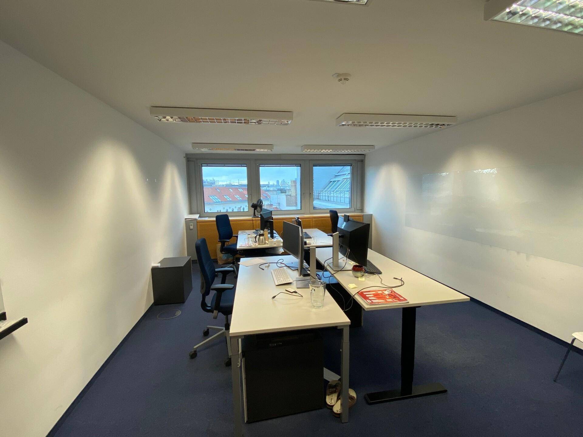 Modernes Einzelbüro mit zwei Arbeitsplätzen, blauer Teppichboden und großen Fenstern für viel Licht.