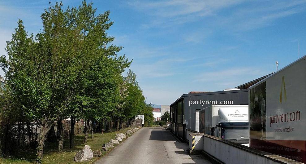 Zufahrtsweg gesäumt von Bäumen und Steinen, der zu den Gewerbegebäuden mit LKW-Parkplätzen führt.
