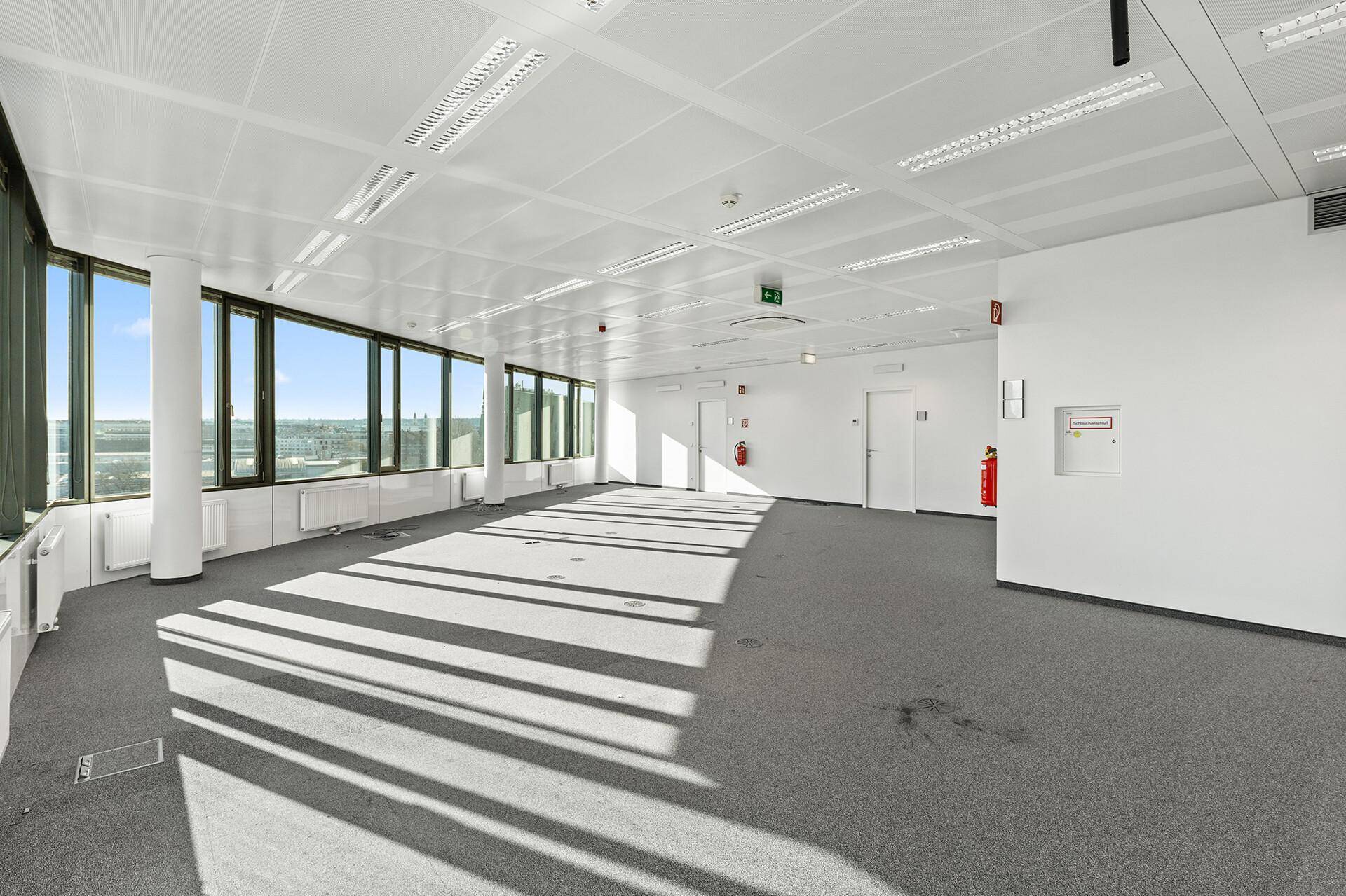 Heller und geräumiger Büroraum mit Teppichboden und weitem Ausblick durch die großen Fenster.
