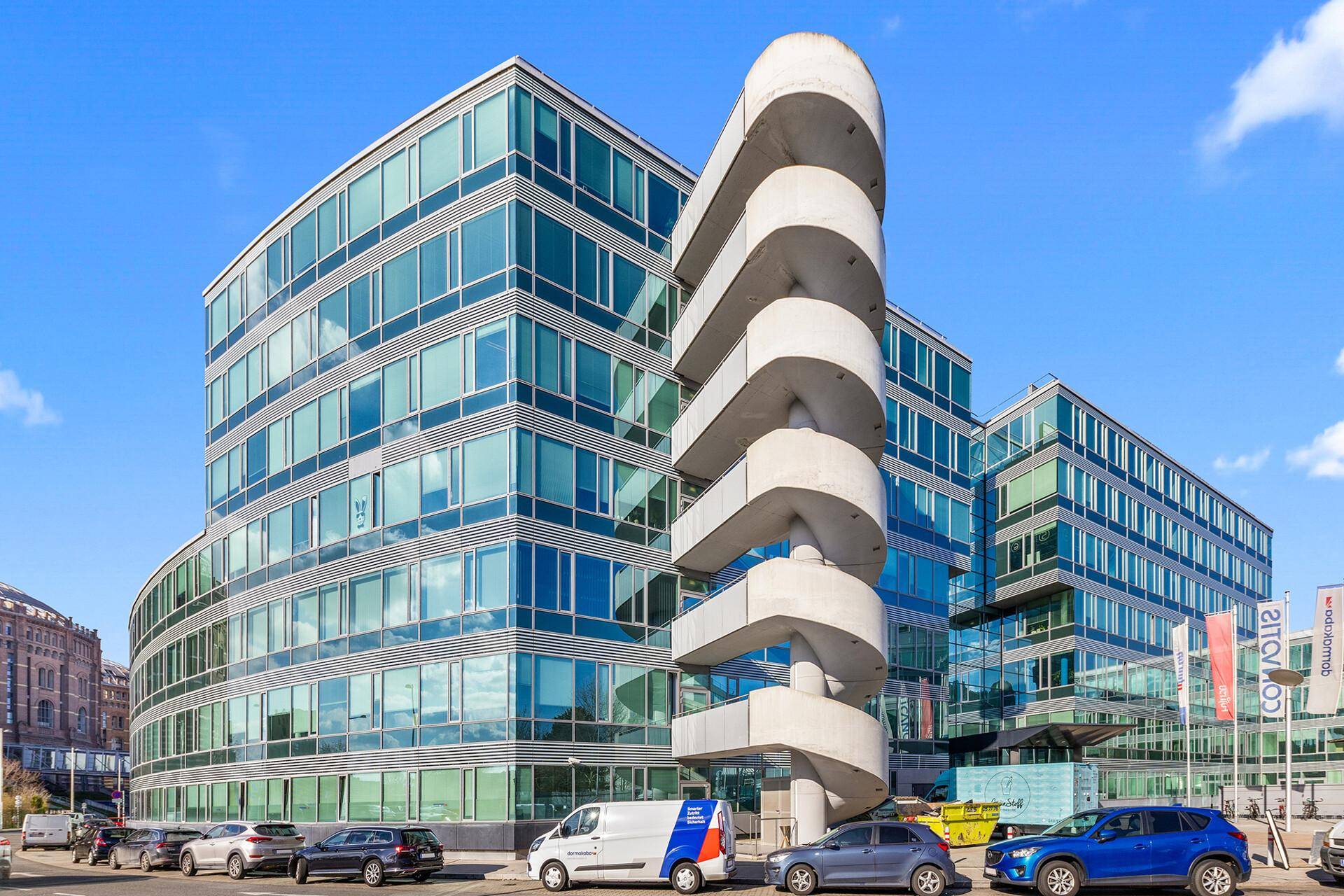 Modernes Bürogebäude mit geschwungener Glasfassade und einer markanten, spiralförmigen Außentreppe.