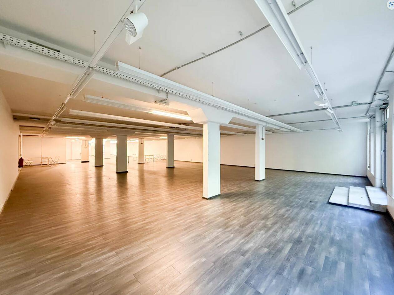 Großer, leerer Gewerberaum mit Säulen, Holzoptikboden und sichtbaren Deckeninstallationen.