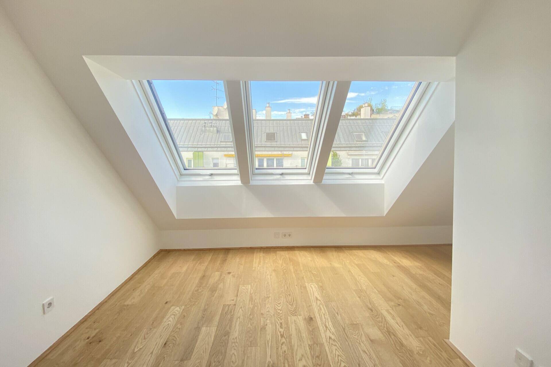 Helles Zimmer im Dachgeschoss mit Holzboden und drei großen Dachfenstern, ideal als Schlaf- oder Arbeitszimmer.