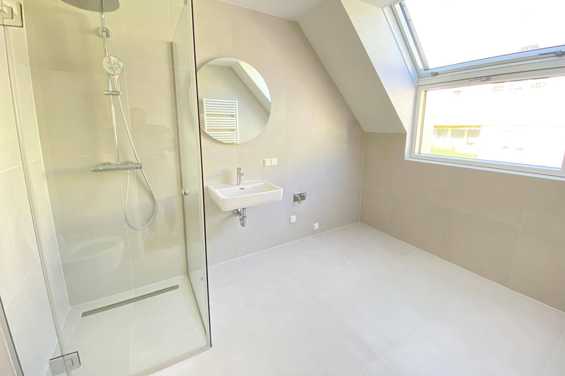 Modernes Badezimmer mit ebenerdiger Dusche, Einzelwaschbecken und beheiztem Handtuchhalter unter einem Dachfenster.