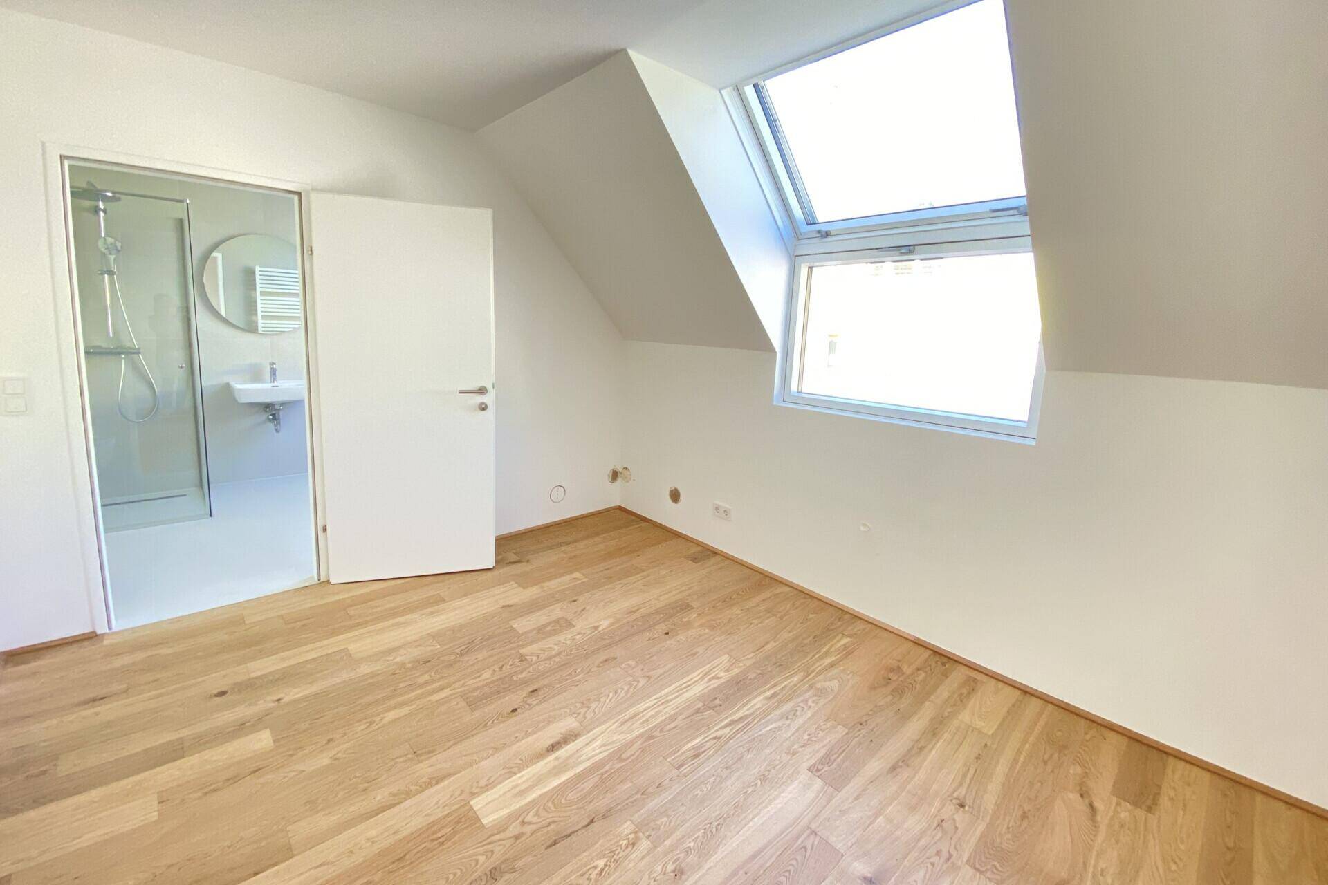 Schlafzimmer mit Holzboden, Dachfenster und direktem Zugang zu einem modernen Badezimmer mit Dusche.