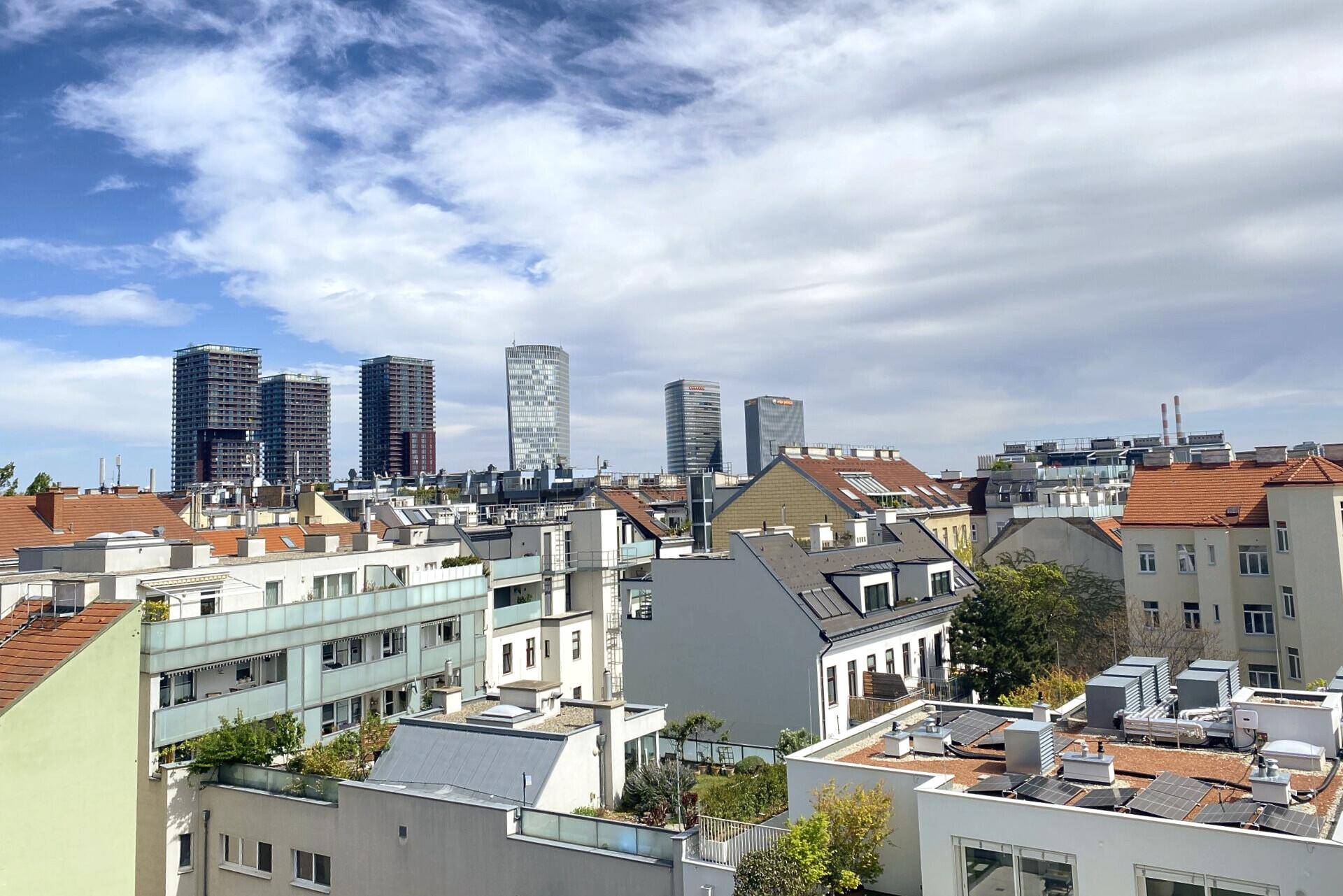 Panoramablick über die Dächer der Stadt mit moderner Skyline im Hintergrund unter blauem Himmel.