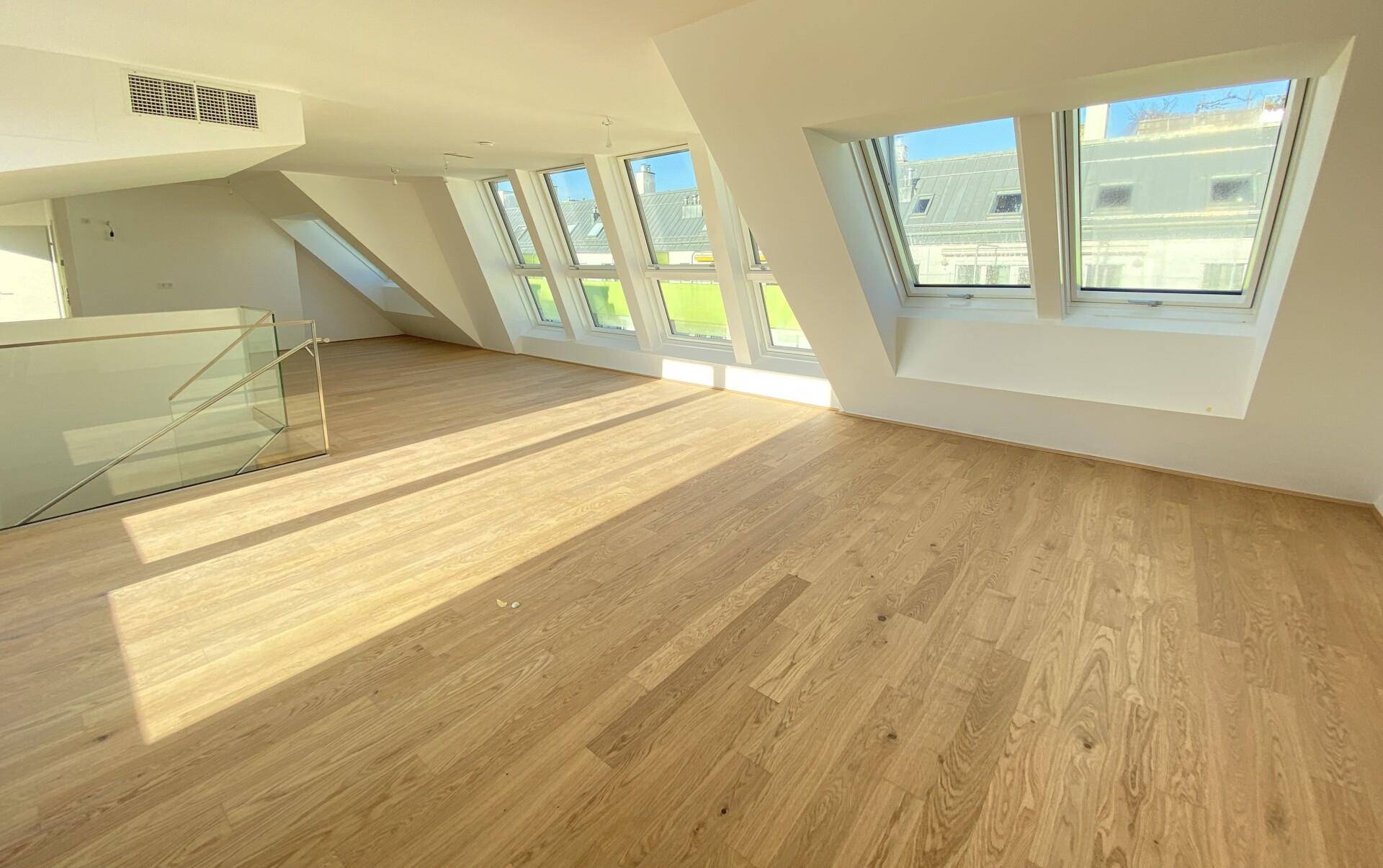 Großzügiger Wohnbereich im Dachgeschoss mit Holzboden, vielen Dachfenstern und moderner Glasbrüstung.