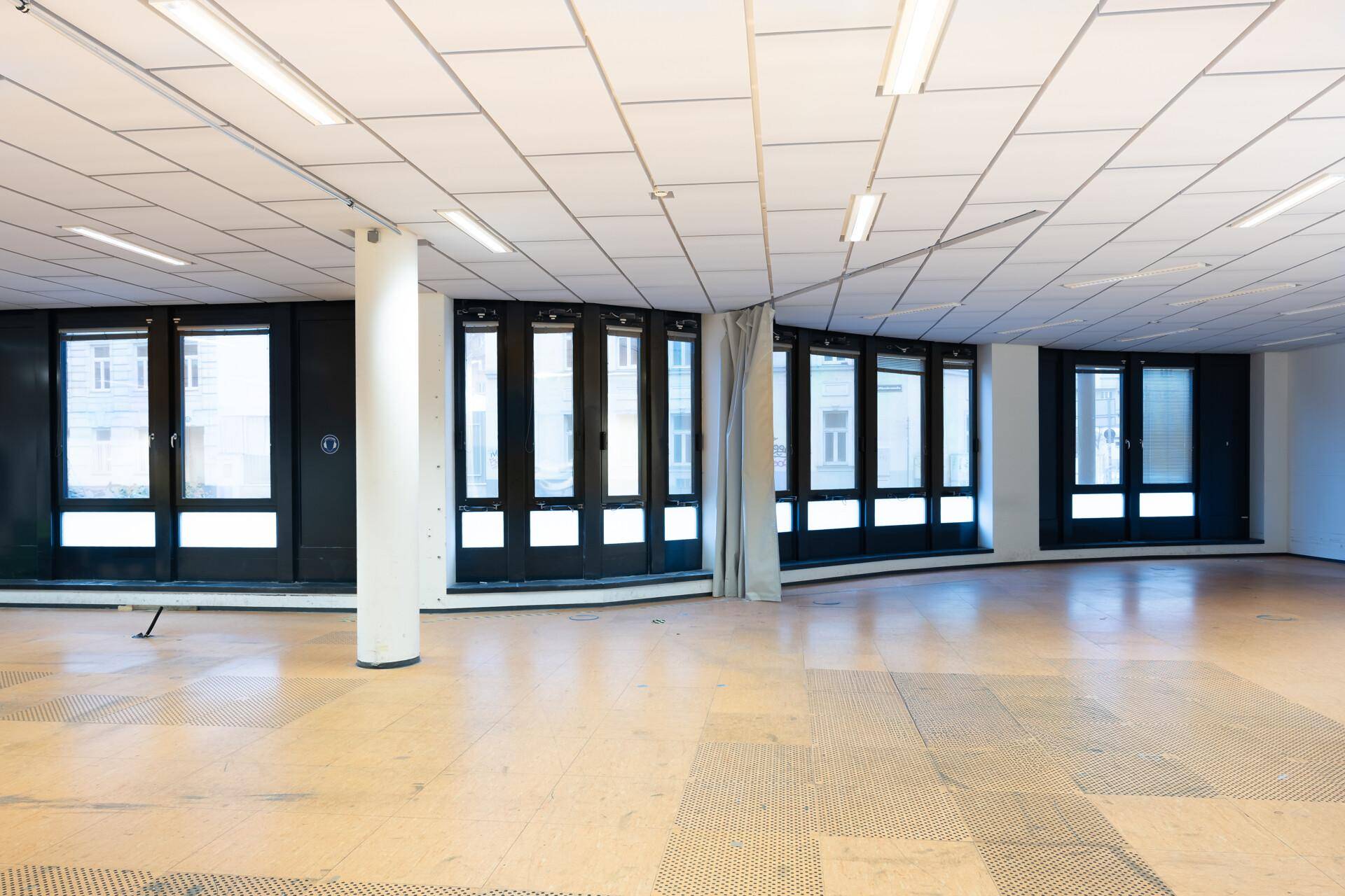 Großer, leerer Großraumbüro-Bereich mit Rasterdecke, vielen geschwungenen Fenstern und hellem Boden.