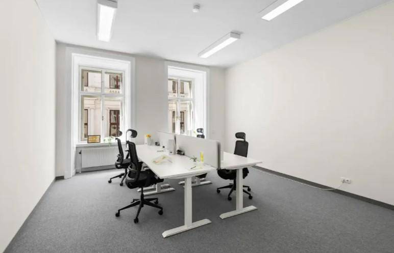 Helles Büro mit zwei Arbeitsplätzen, Teppichboden und großen Fenstern zur Straße.