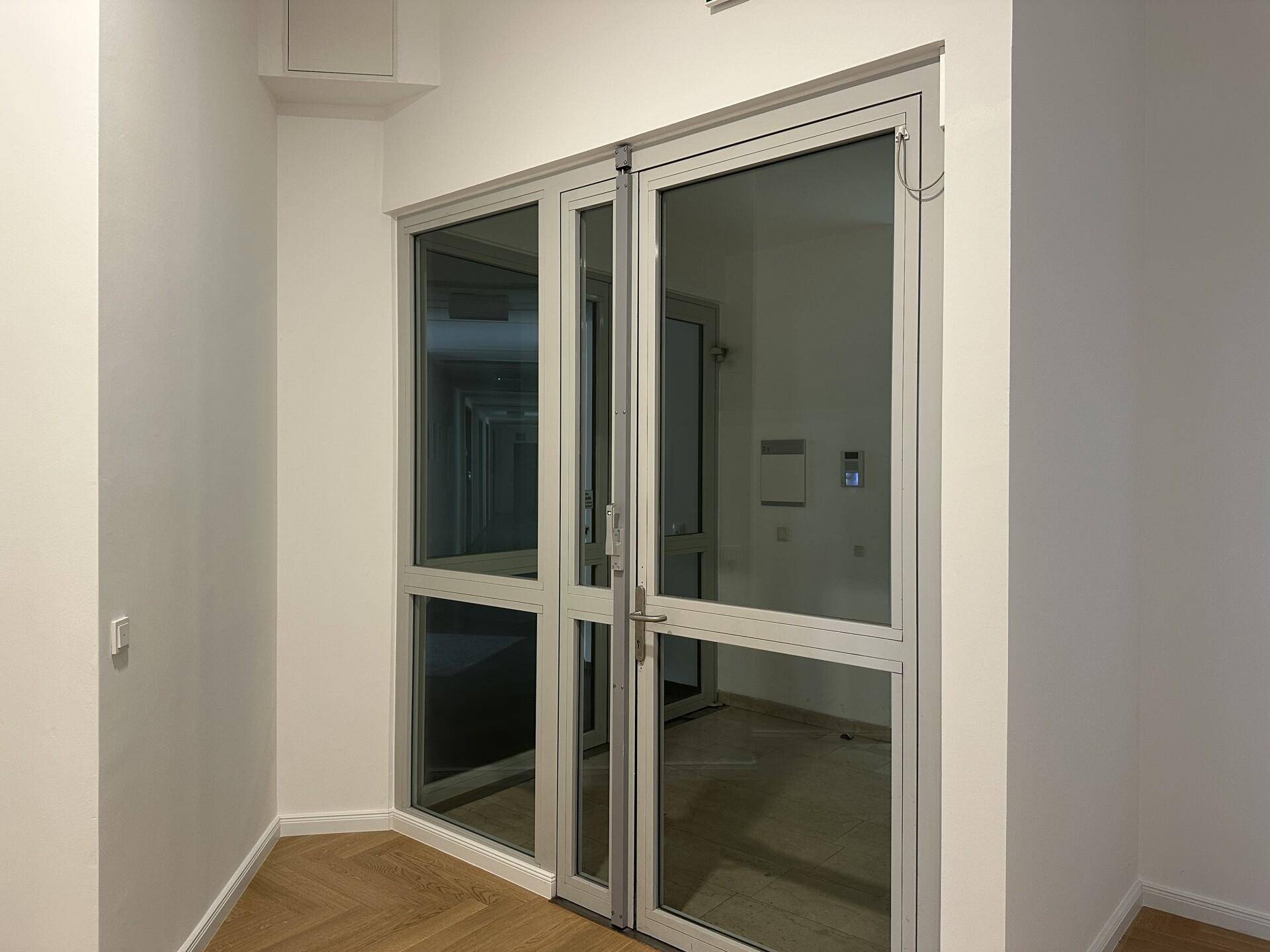 Heller Flur mit Glasdoppeltüren, die zu weiteren Räumen oder einem Treppenhaus führen.