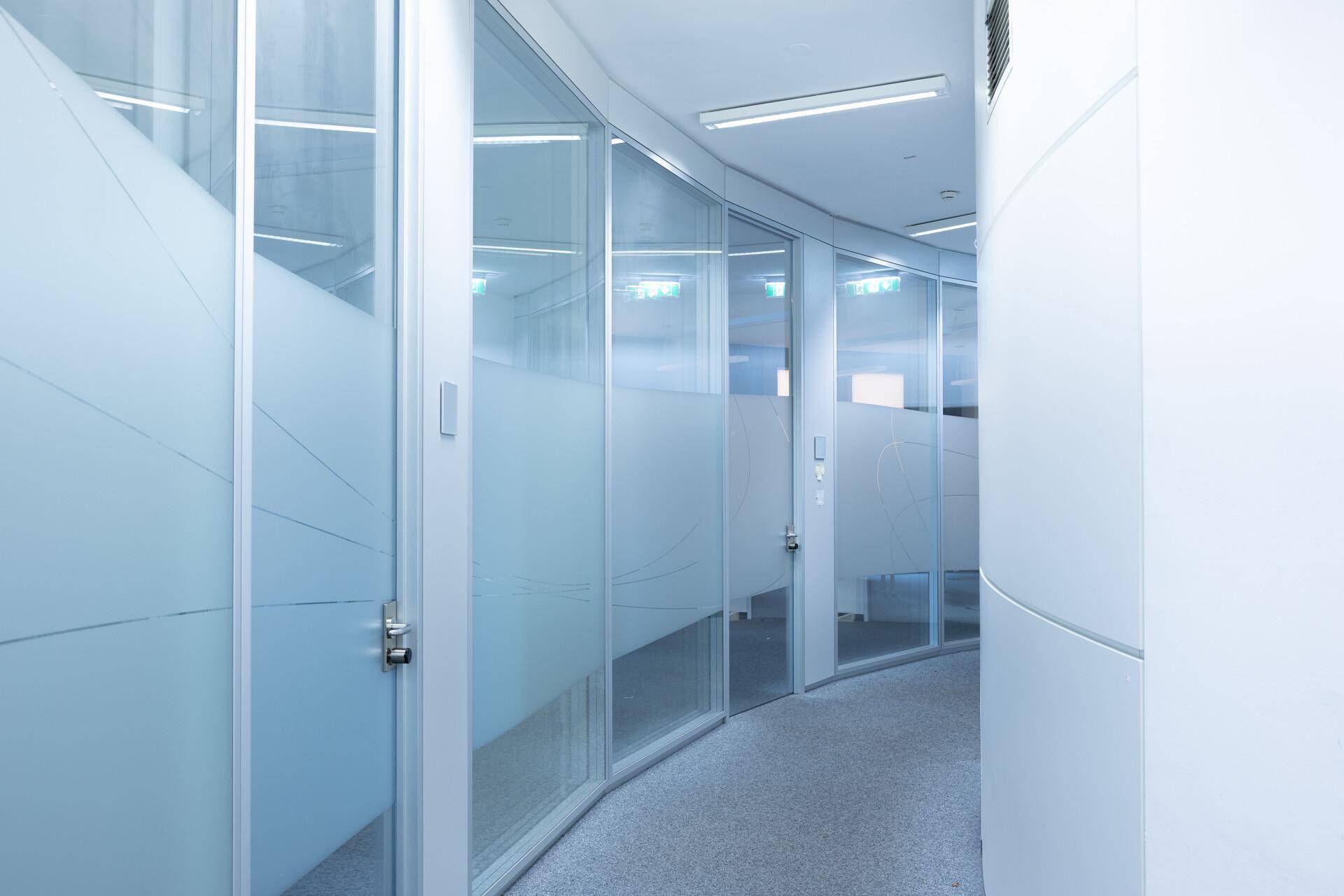 Moderner Bürogang mit Glaswänden und Milchglasfolien für Privatsphäre.