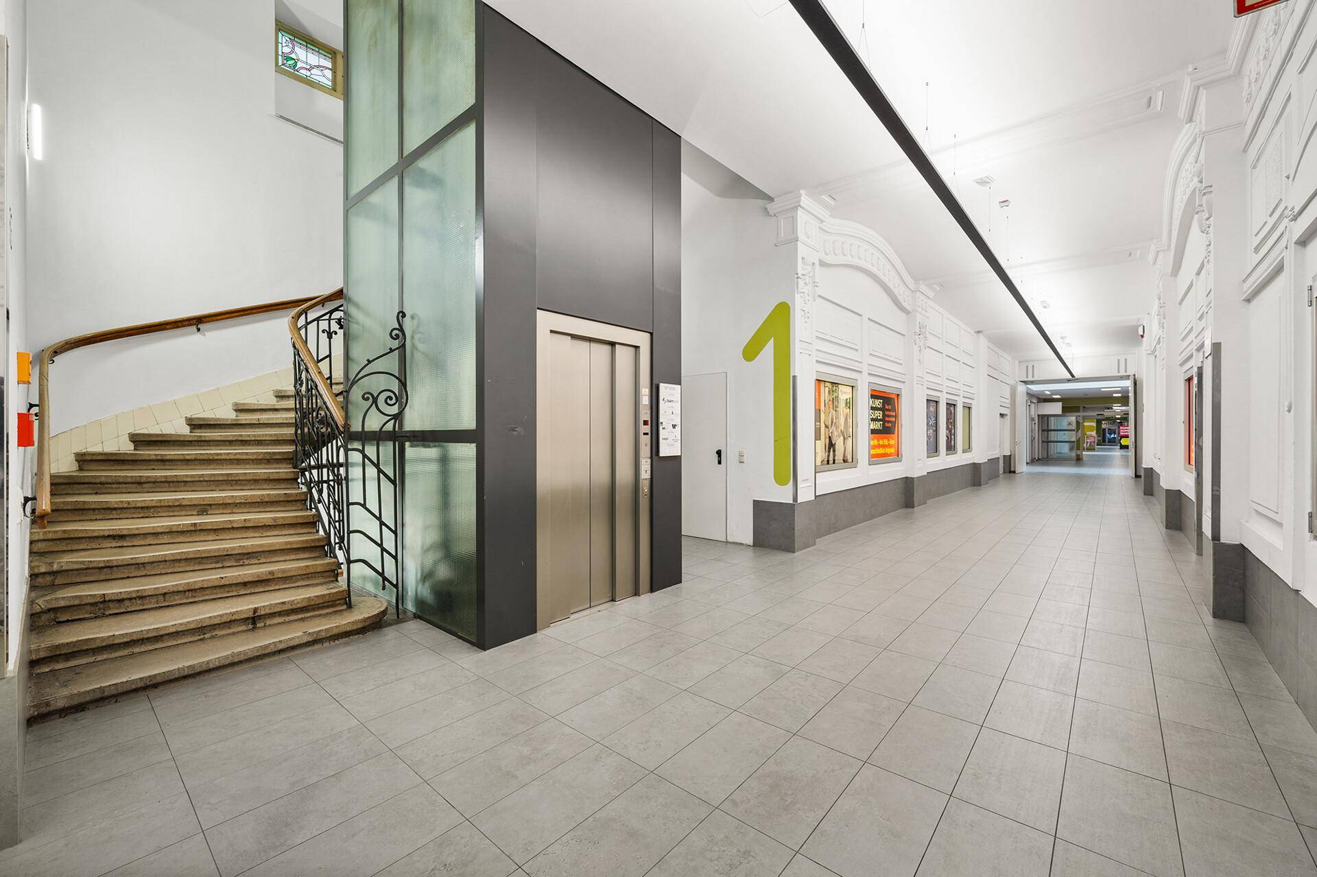 Moderner Eingangsbereich mit elegantem Treppenhaus, Glasaufzug und hellem Flur mit Fliesenboden.