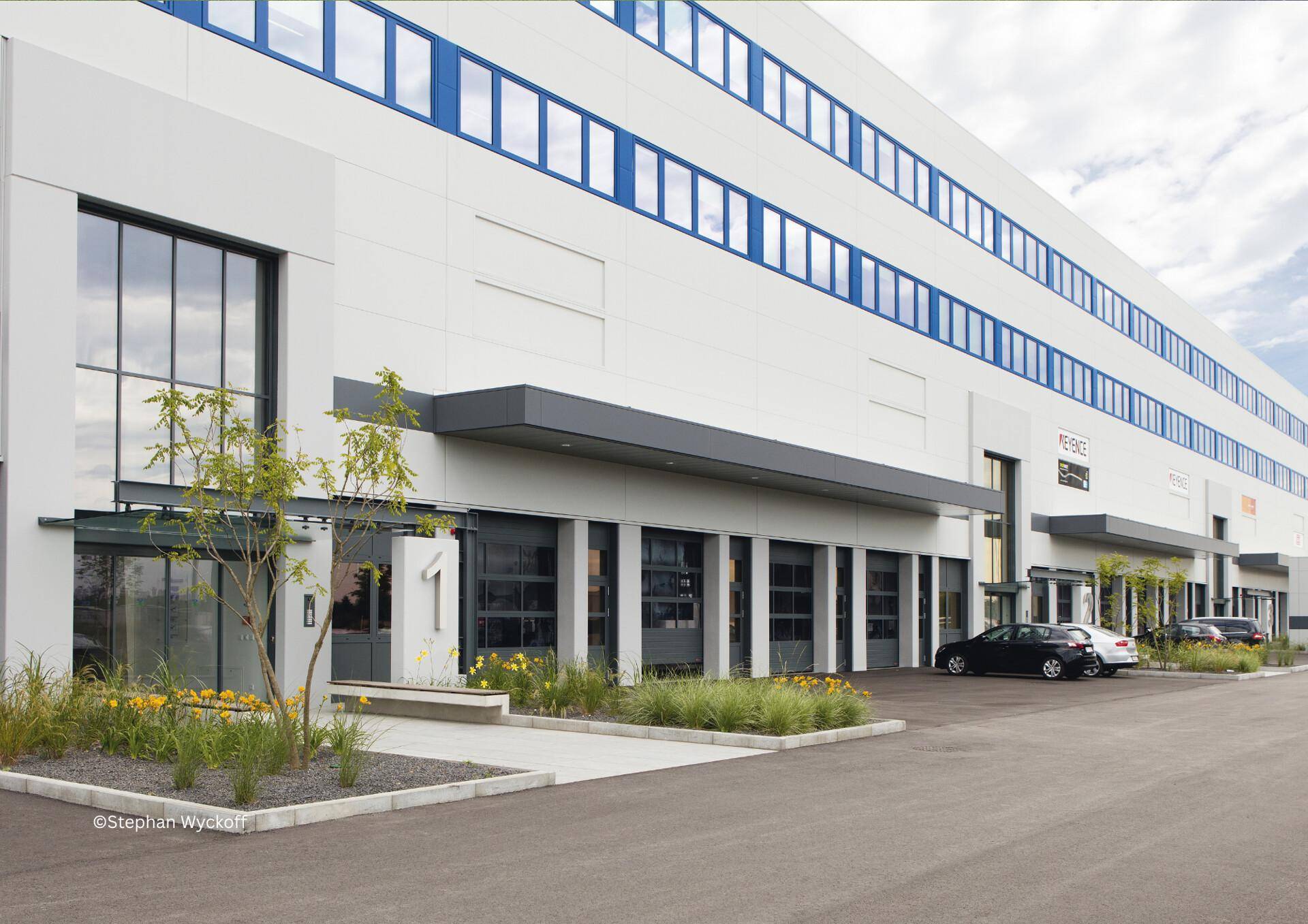 Lange Fassade eines modernen Geschäftsgebäudes mit vielen Fenstern und Parkplätzen.