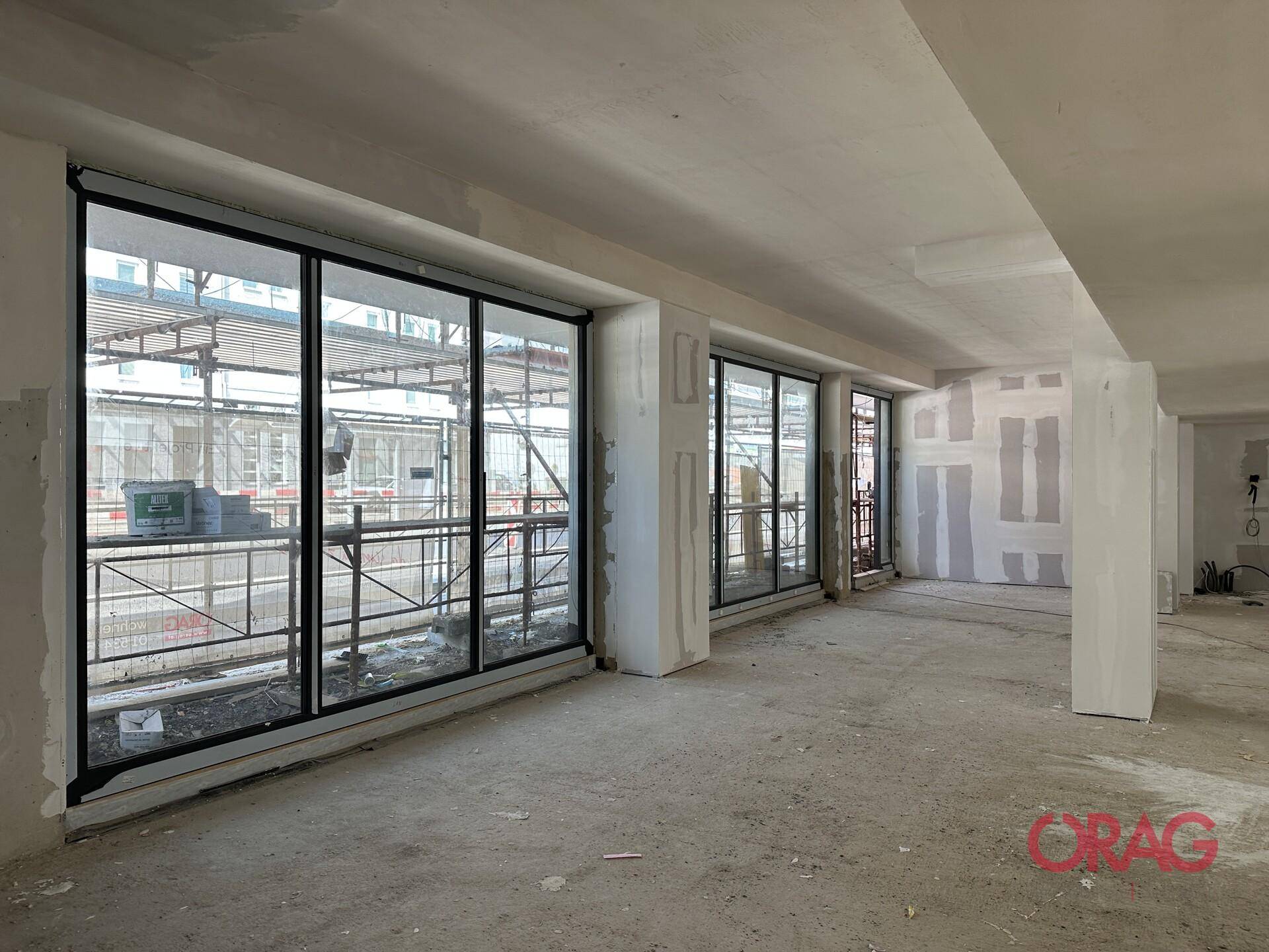 Großer, offener Innenraum im Rohbau mit weiten Fensterfronten und Blick auf Baugerüst.