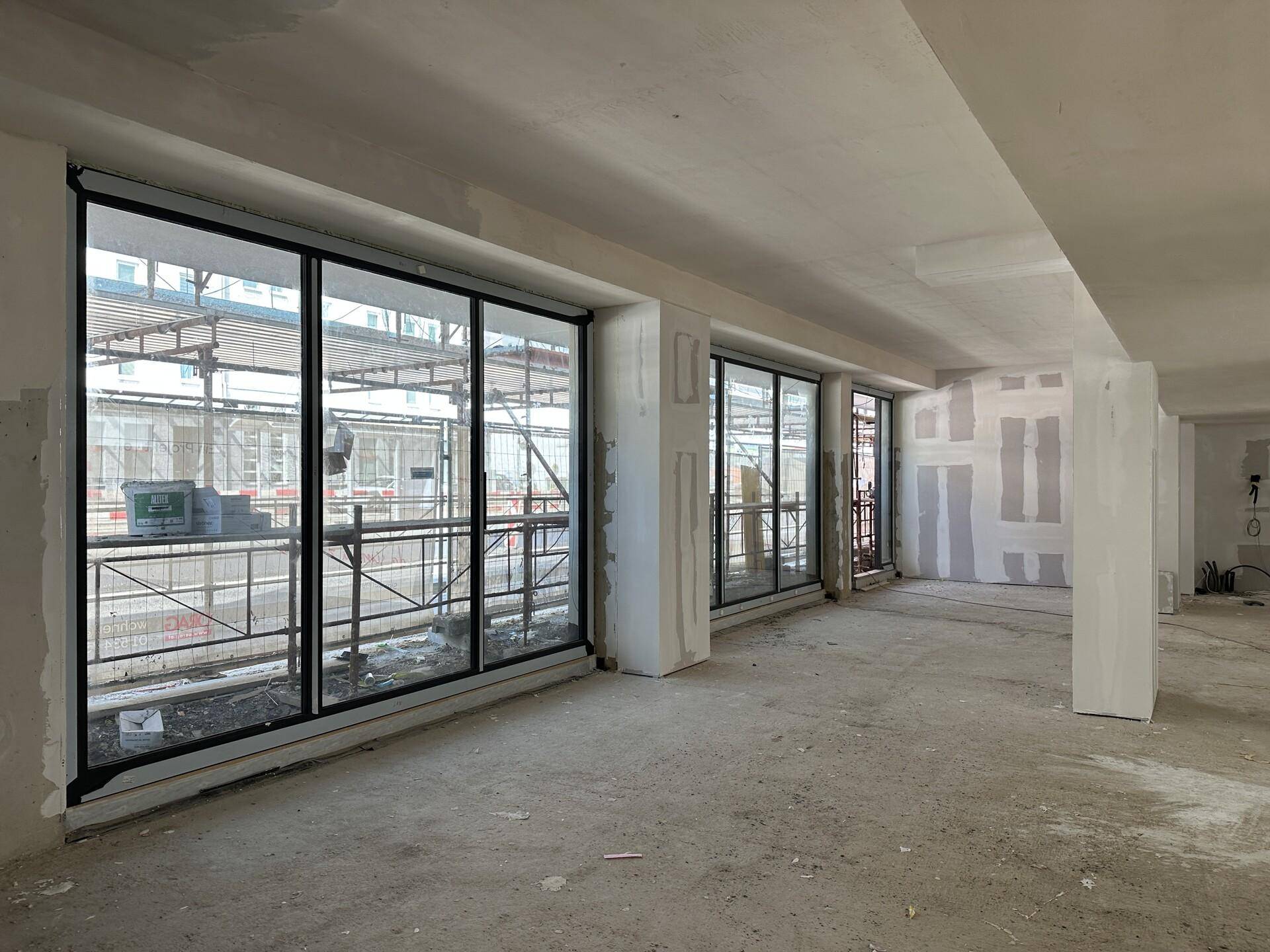Unfertiger Innenraum mit großen Fenstern und Blick auf Baugerüste, bereit für den weiteren Ausbau.
