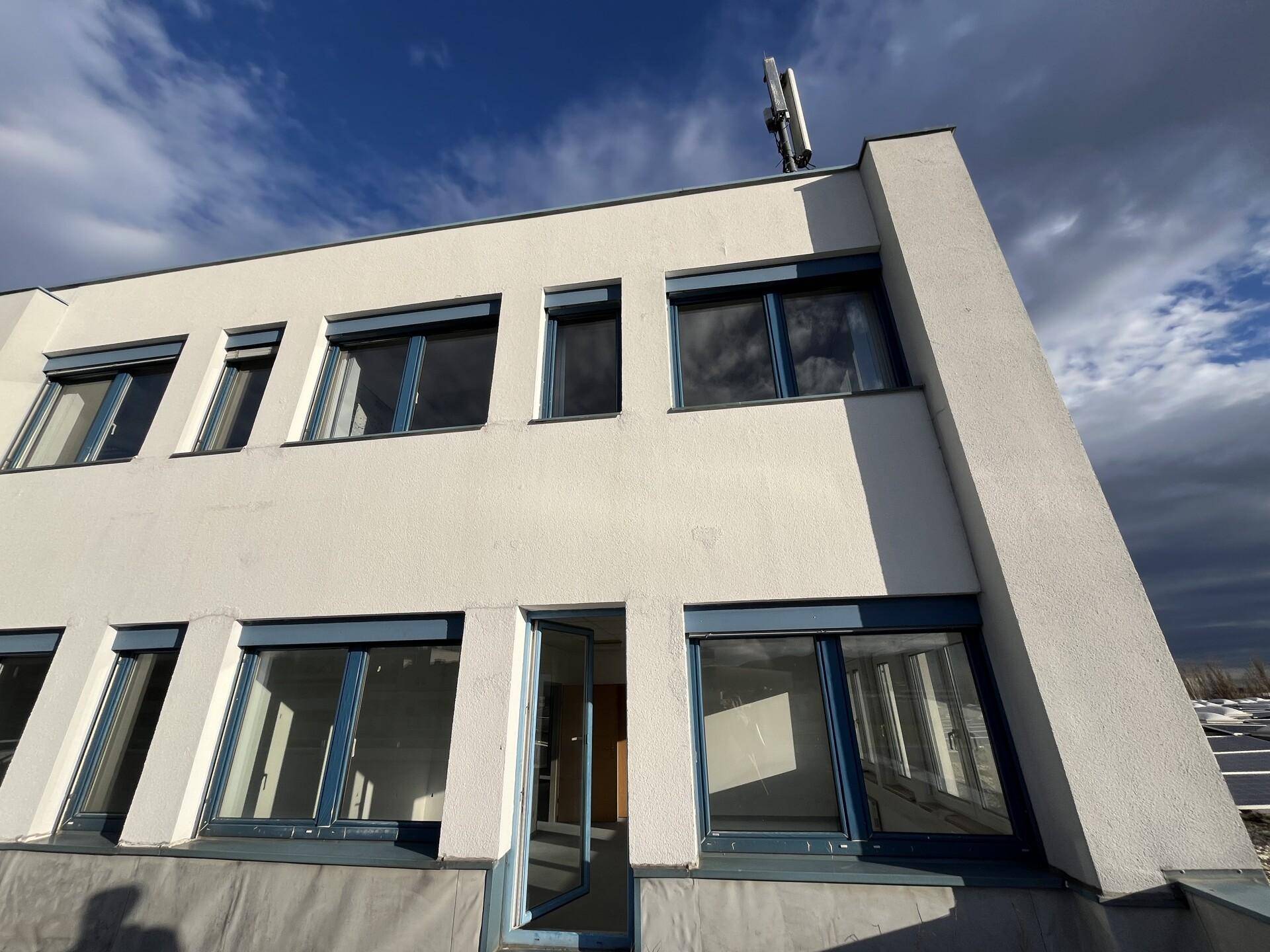 Seitenansicht eines modernen Gebäudes mit blauen Fensterrahmen, Rollläden und einer schrägen Fassade.
