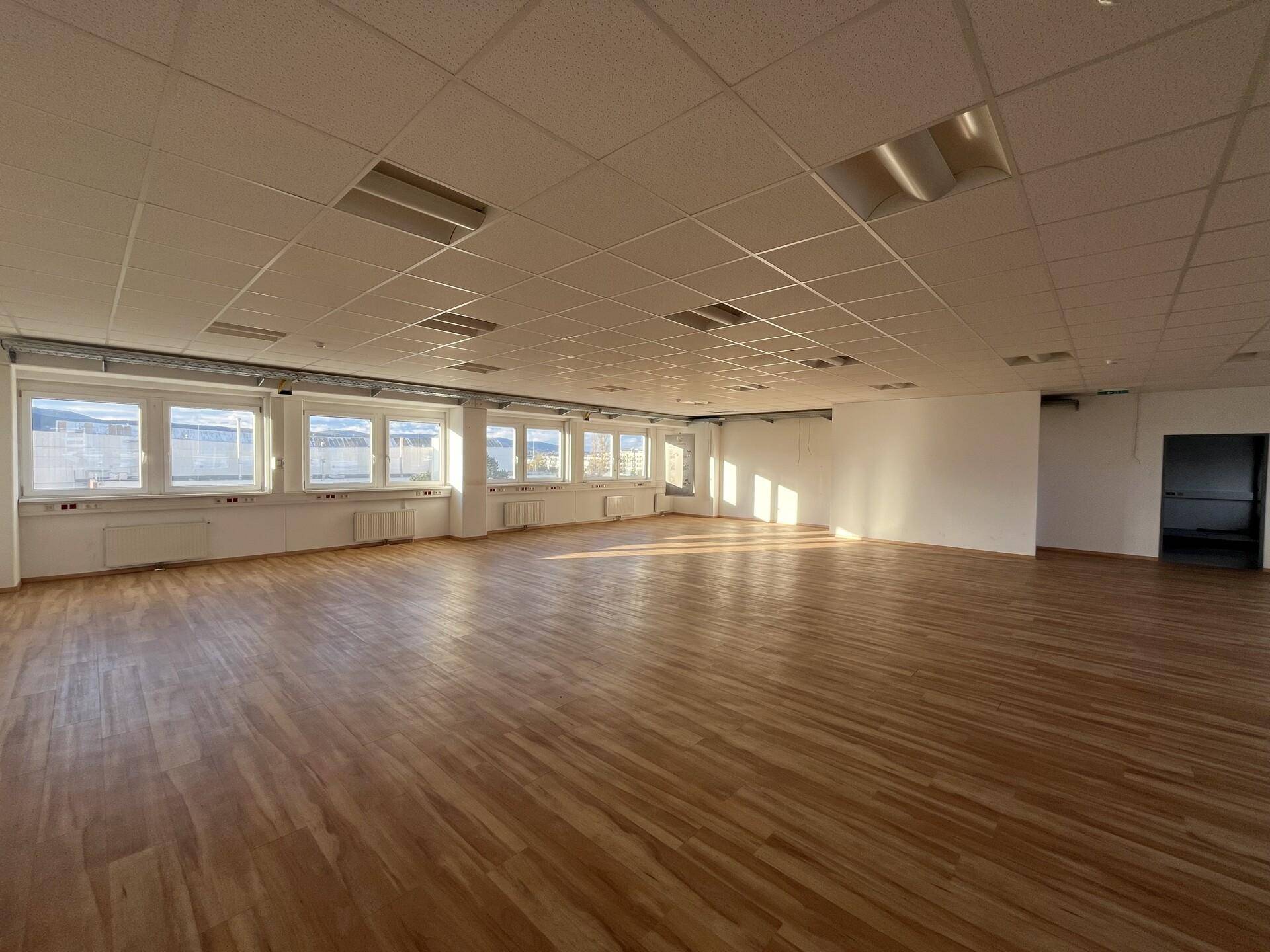 Großer, heller Raum mit Holzparkettboden und vielen Fenstern, ideal für verschiedene gewerbliche Nutzungen.