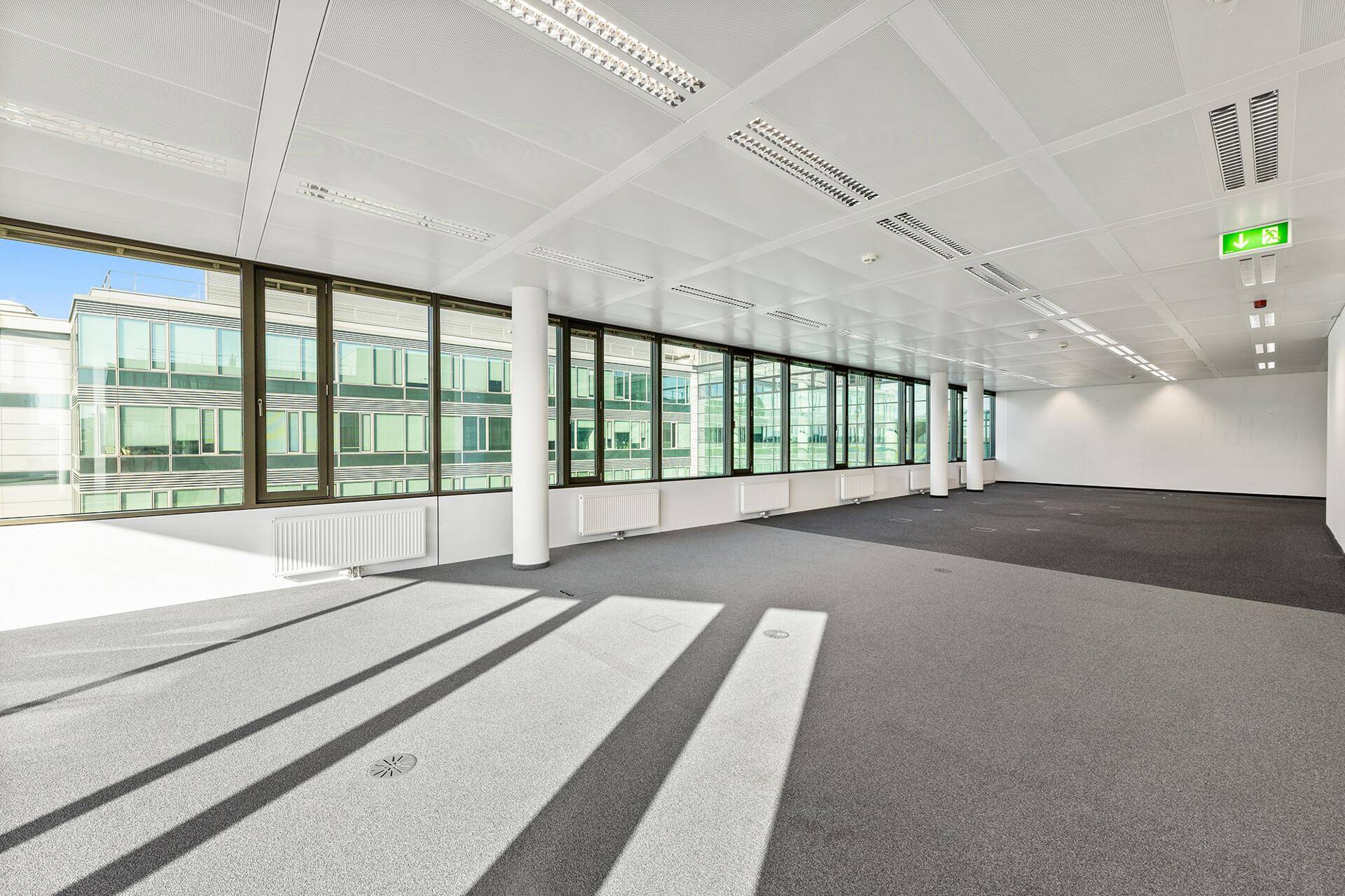 Helles, leeres Büro mit großen Fensterfronten und Blick auf ein gegenüberliegendes modernes Gebäude.